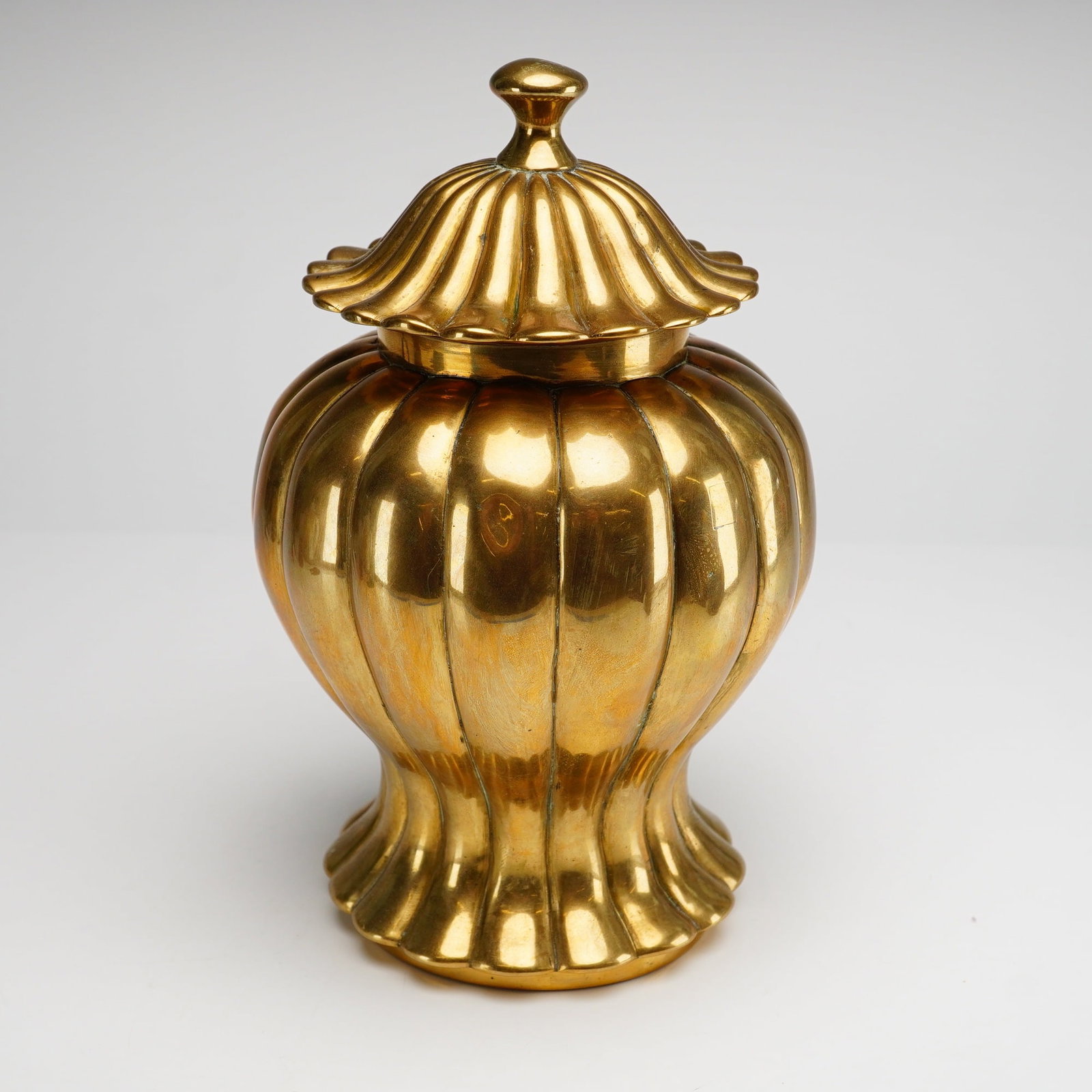Lidded Brass Jar with Ribbed Decoration: This lidded brass canister, frequently referred to as a ginger jar or melon jar, is constructed from cast and polished brass. The vessel features a prominent lobed form with deep vertical fluting that