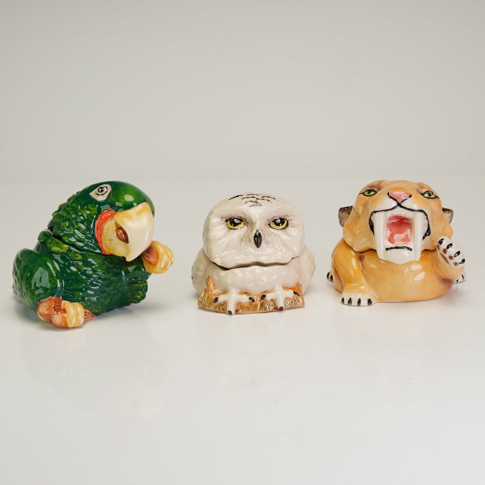 3pc Kevin Francis Lidded Face Pots, John the Parrot, Harold, and Claw the Sabre Tooth: The set includes John the Parrot (2003), a vibrant green parrot inscribed with the Monty Python reference Its not dead, Its just resting; Harold the Owl (2002), a snowy owl inscribed with the