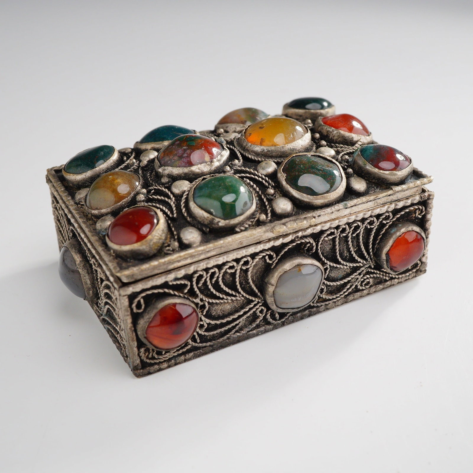 Ornate Filigree White Metal Trinket Box with Mixed Gemstones: This rectangular miniature trinket or jewelry box features intricate filigree wirework in scrolling and foliate patterns across the lid and all four sides. The exterior is heavily embellished with mul