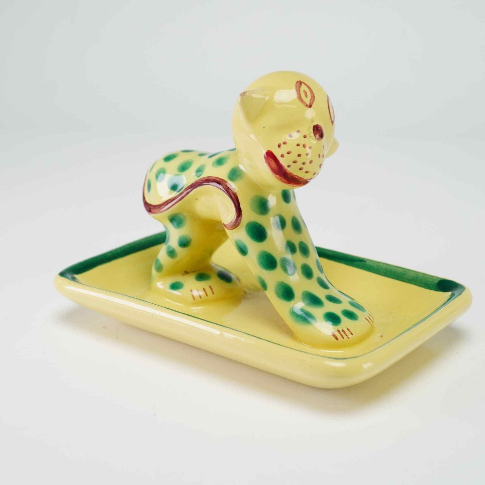 French Hand Painted Ceramic Leopard Jewelry Tray: This hand-painted ceramic trinket tray or ring holder features a rectangular base with a pale yellow ground and a green-painted interior border. A stylized leopard figurine is centered in an arched