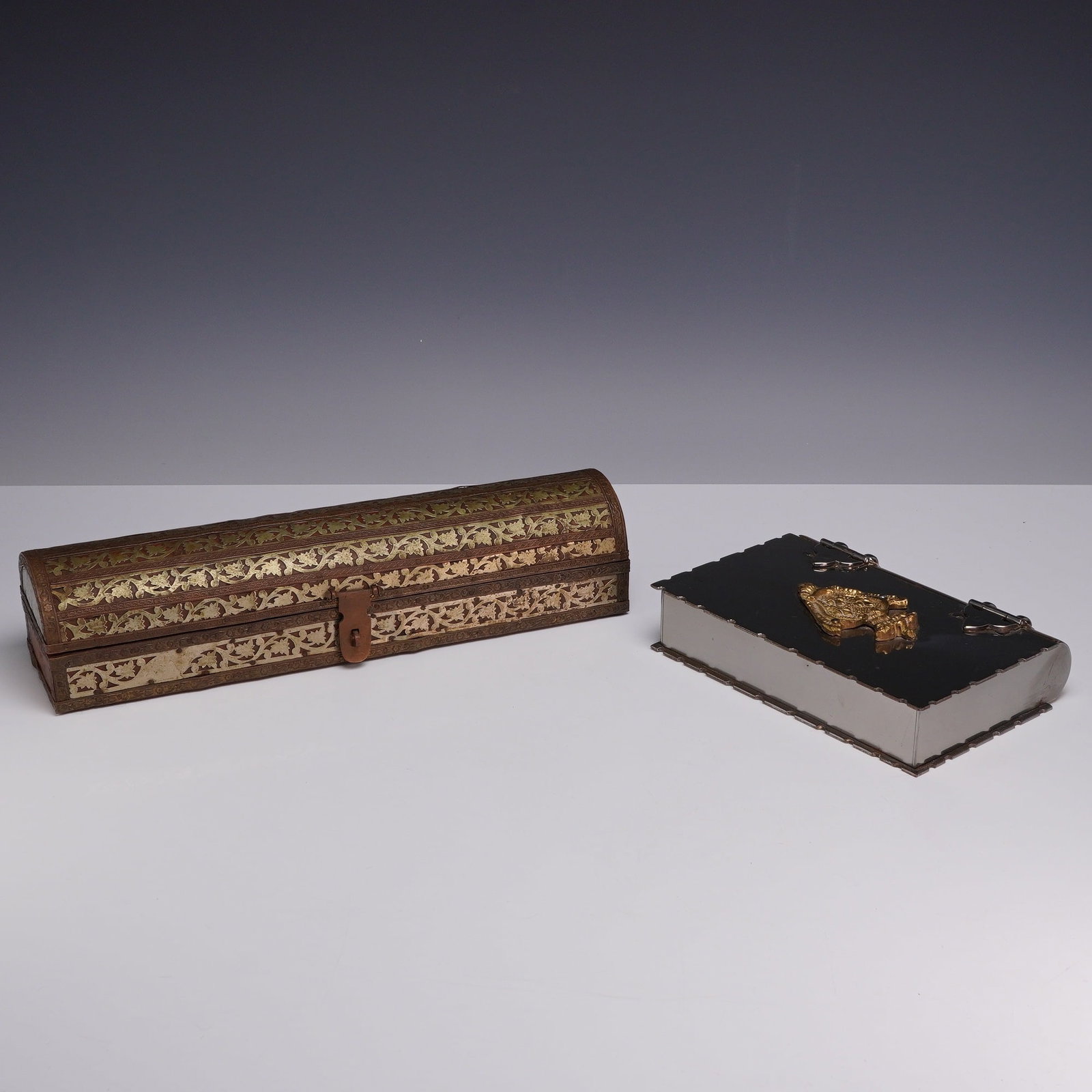 Two Storage Boxes including Brass Qalamdan and Italian Book-form: This lot consists of two decorative storage containers. The first is an ornate wood and brass qalamdan, a traditional pen box, featuring an elongated rectangular form with a domed hinged lid and a