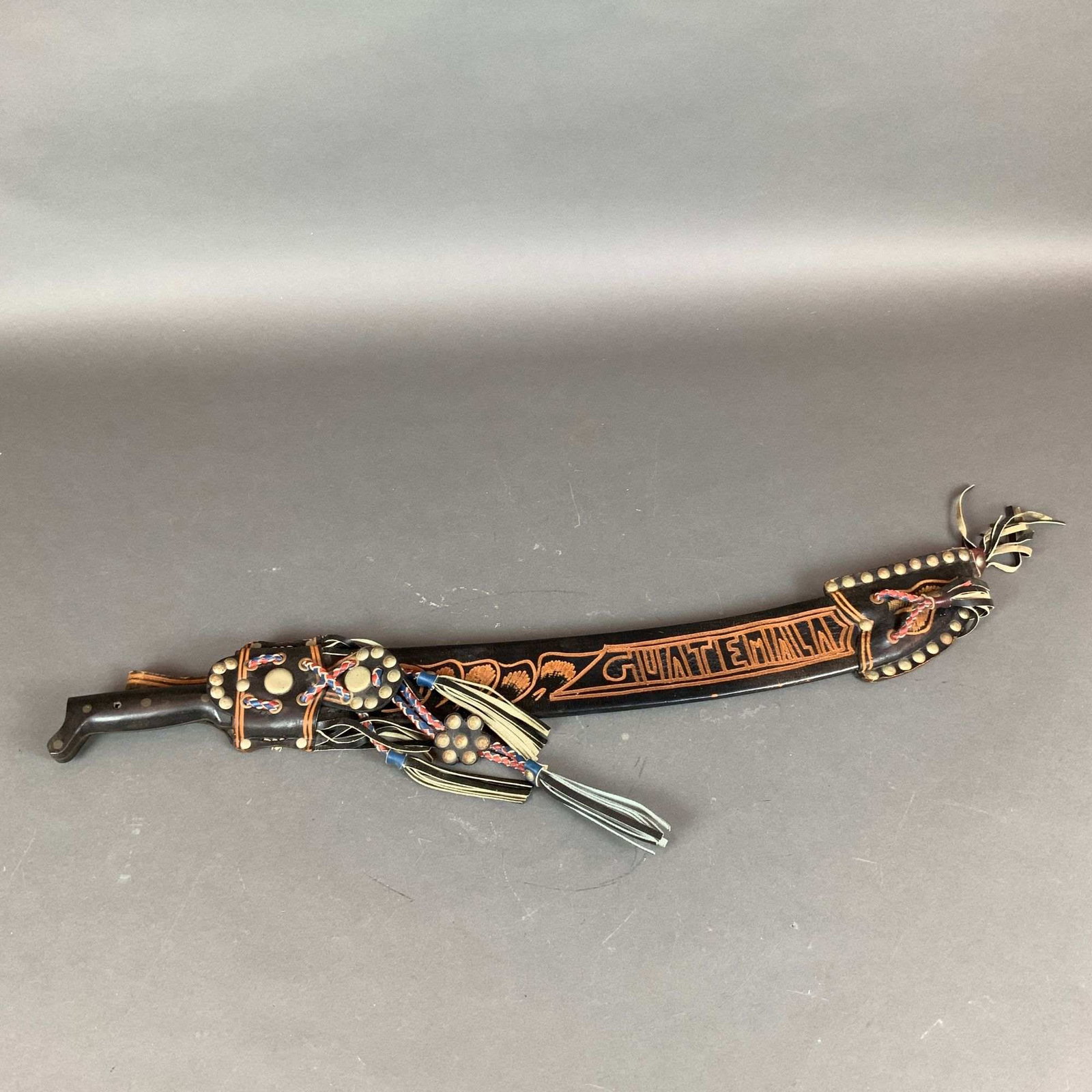 Guatemalan Corneta Machete No. 127 with Tooled Leather Sheath: This lot features a vintage Central American machete with a decorative tooled leather sheath. The steel blade is stamped with a trumpet logo and the brand name CORNETA. Below the logo, the text reads 