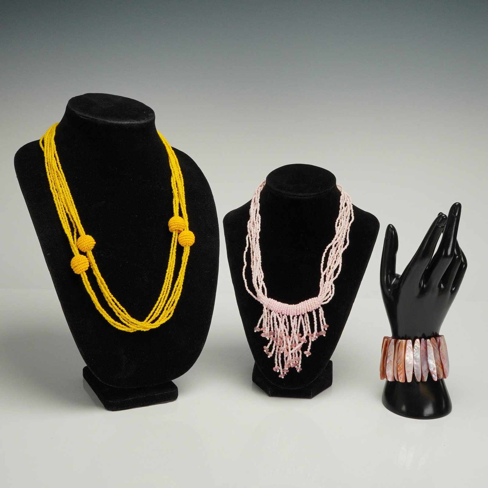 A Trio of Contemporary Beaded Necklaces and Shell Cuff Bracelet Set: The lot consists of a trio of contemporary costume jewelry pieces, including two beaded necklaces and one bracelet. The first necklace is a multi-strand design constructed from bright yellow seed bead
