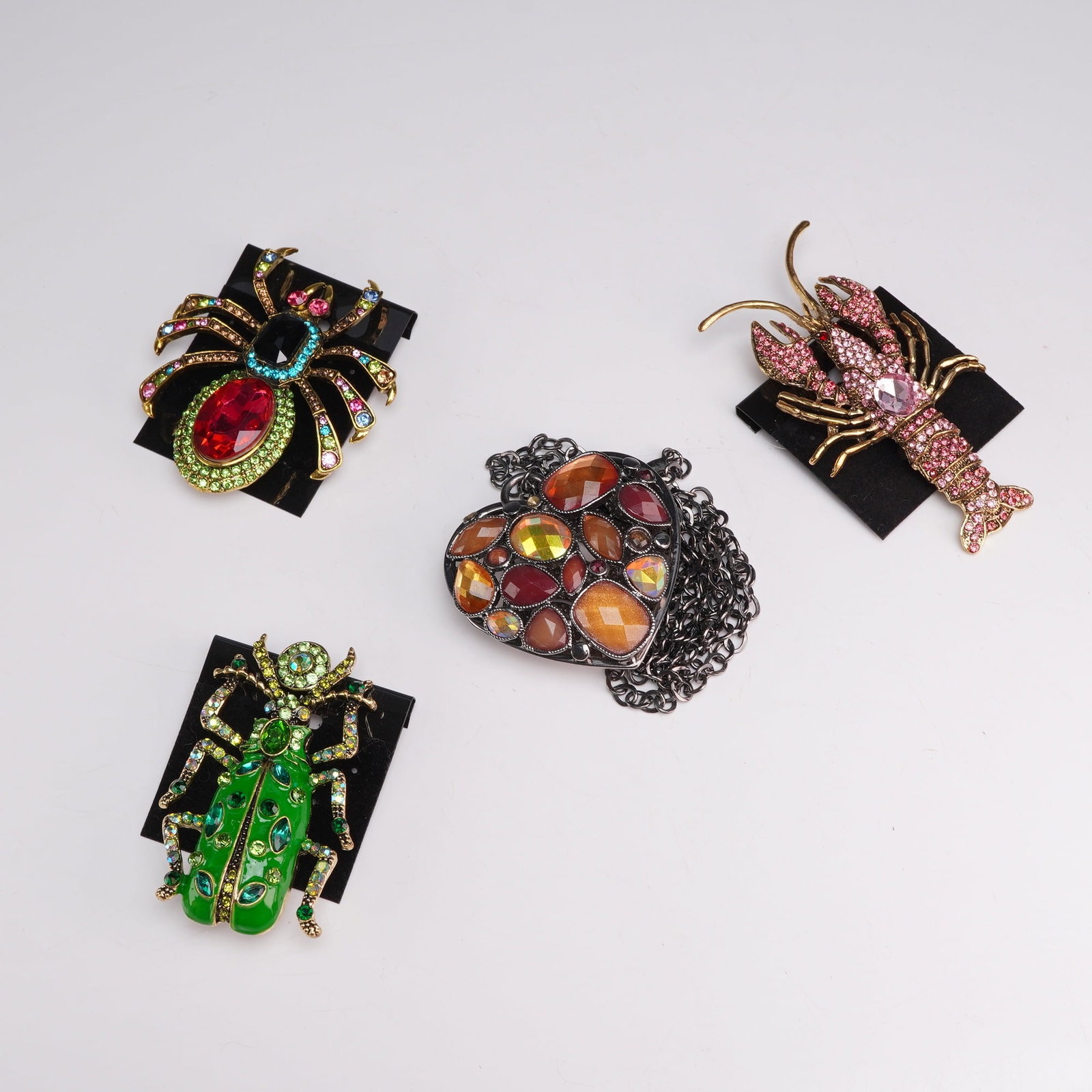 4pc Costume Jewelry Featuring Animal Brooches and Heart Pendant Necklace: The first item is a spider brooch made of gold-tone base metal, featuring a central red oval faceted glass stone on the abdomen surrounded by a border of green rhinestones. The thorax is set with a bl