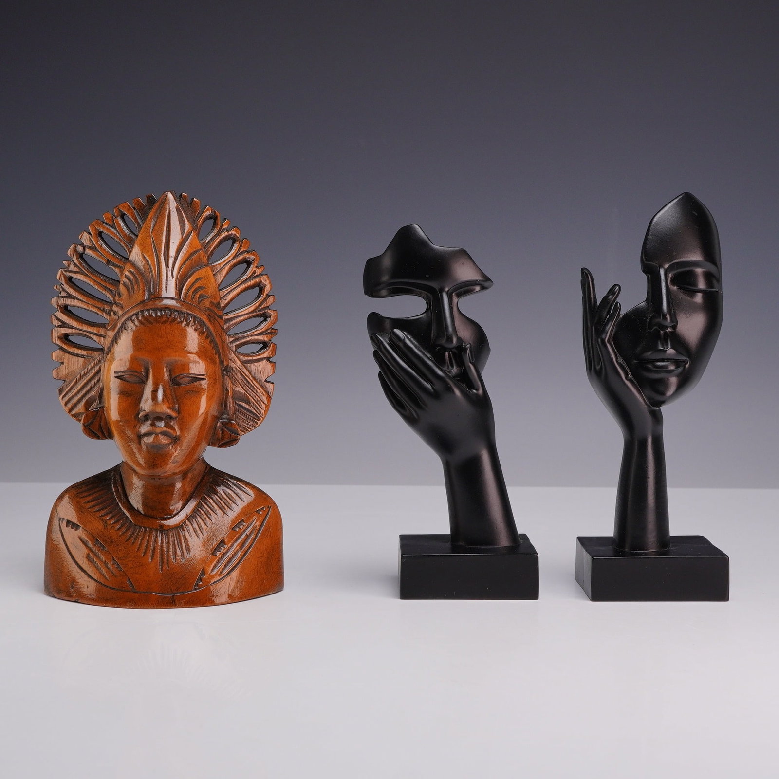 Three Balinese Carved Wood Bust and Thinker Statues: The collection includes a Balinese Bust sculpture carved from a polished reddish-brown hardwood. The bust depicts a figure with a serene expression and a prominent, radiating openwork headdress. Also 