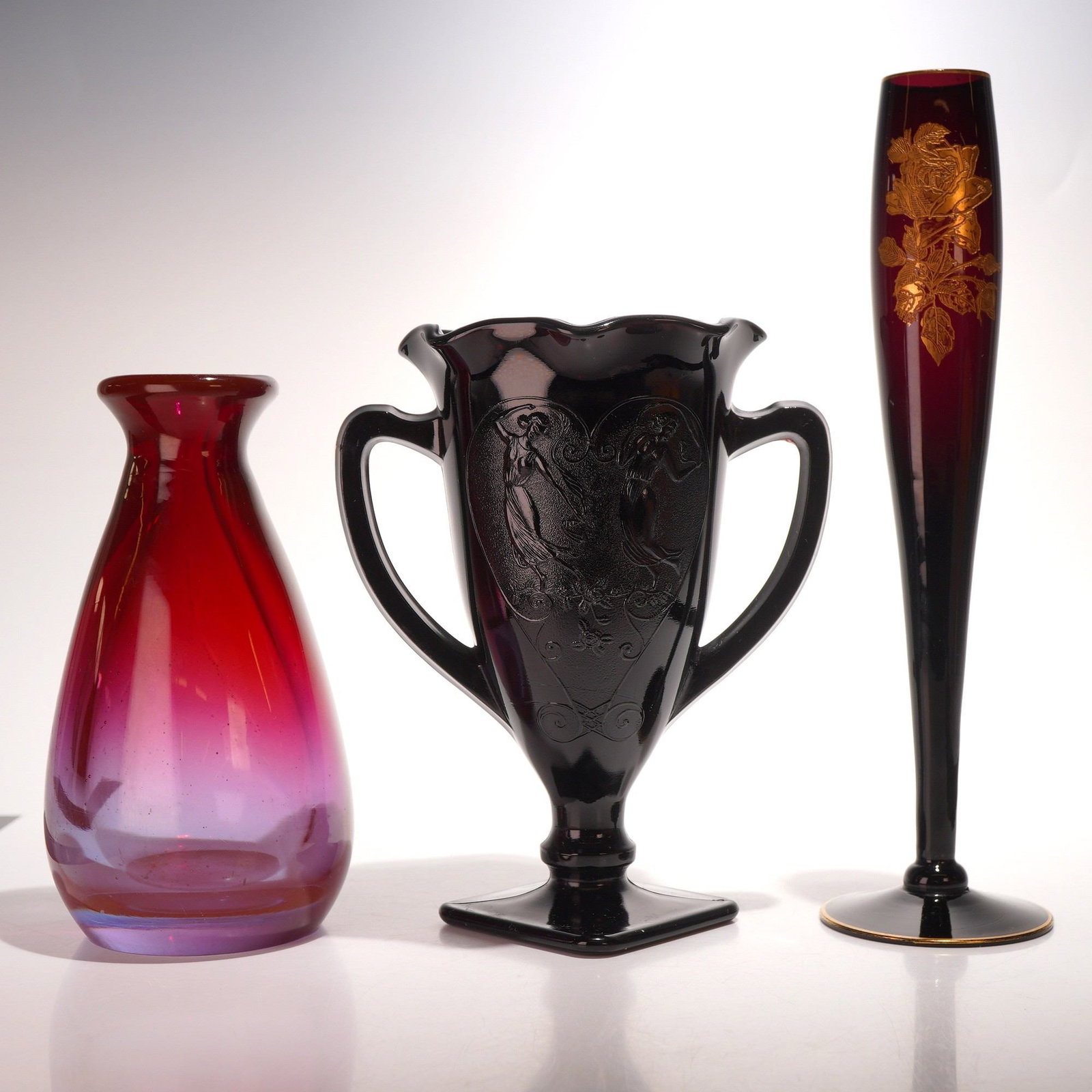 3pc Black Amethyst, Floral Bud, and Red Glass Vases: A curated collection of three vintage glass vessels featuring various colors and techniques. The primary piece is an L.E. Smith black amethyst glass trophy-style vase. This pressed glass item appears 