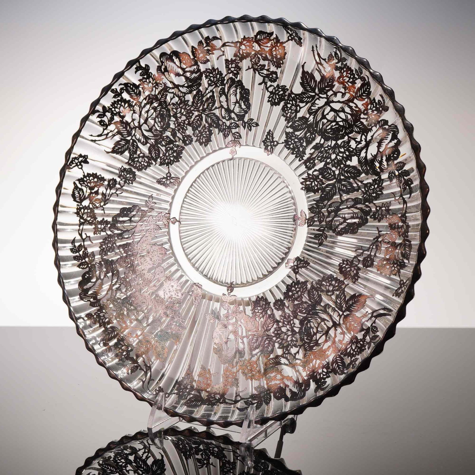 Heisey Glass Silver Overlay Rose Pattern Fluted Platter: This circular pressed clear glass platter features a radially fluted body and a scalloped rim. The piece is decorated with a fine silver overlay depicting a continuous border of trailing roses and