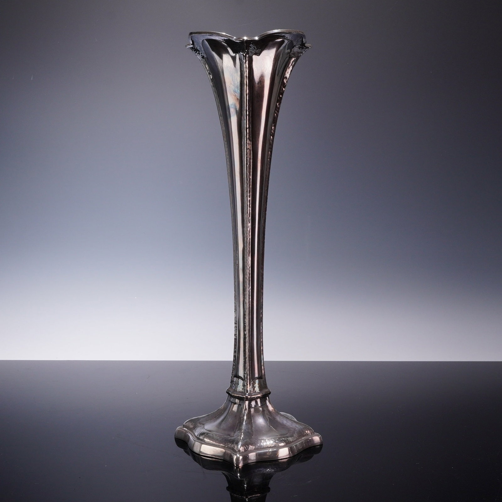 Meriden Silver Plate Company Silver Plated Trumpet Vase Pattern 594: The design consists of an elongated trumpet form with a fluted body flaring at the rim to a four-lobed, ruffled edge. The stem tapers down to a weighted, stepped base with a corresponding lobed and sc
