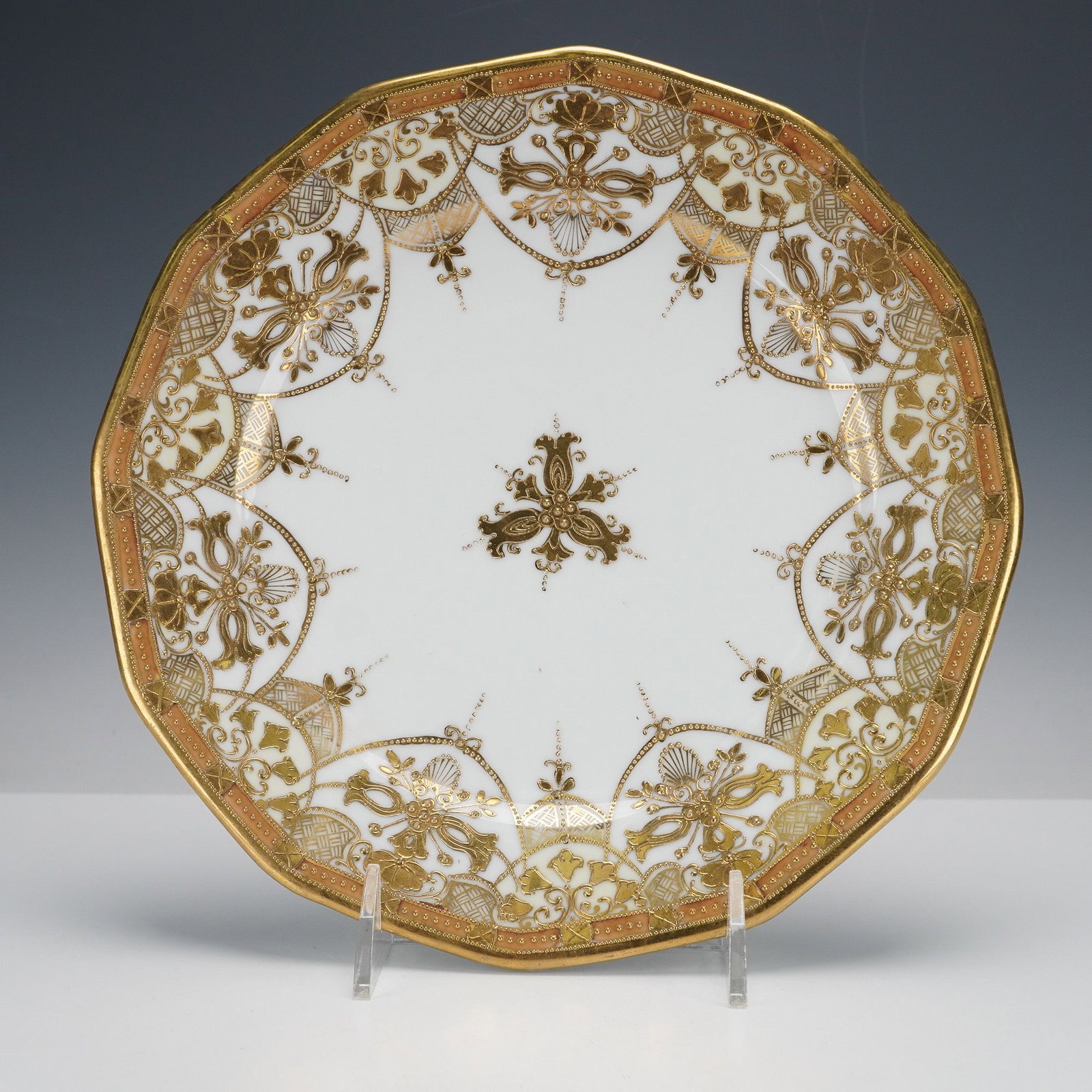 Nippon Hand Painted Raised Gold Octagonal Plate with RC Mark: A Nippon hand-painted raised gold octagonal plate that features an ornate, heavily gilded design against a white ground. A peachy-orange rim band is adorned with a fine lattice pattern in gold. The