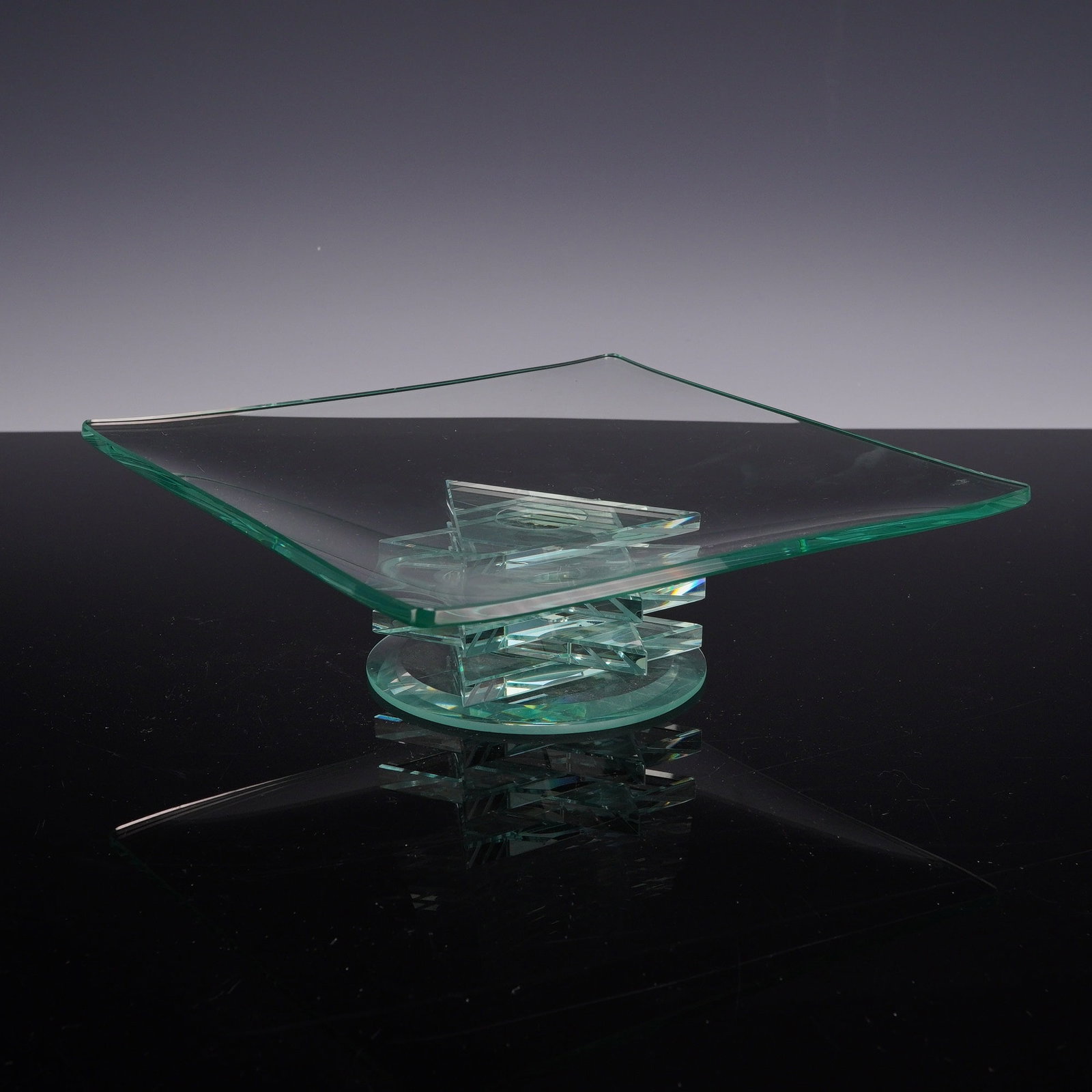 Star of David Glass Pedestal Plate: A contemporary architectural glass centerpiece plate featuring a square slumped glass top with a shallow concave well. The piece is elevated by a geometric base composed of laminated layers of thick p