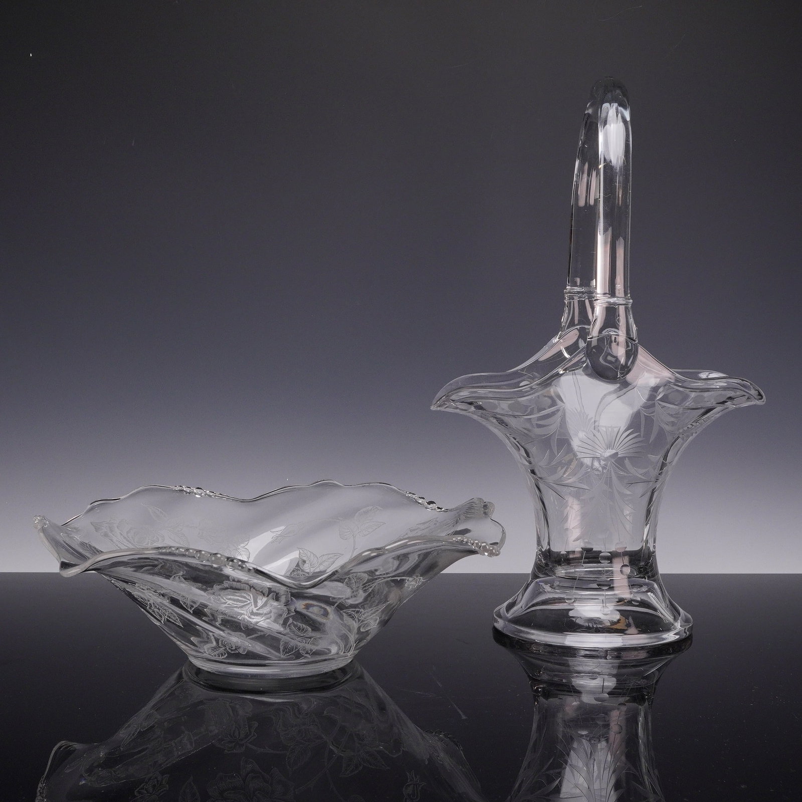 Two Floral Accent Heavy Glass Pieces Including a Tall Handled Basket and a Ruffled Bowl: This lot features two pieces of clear etched elegant glass from the mid-20th century. The collection consists of one tall footed basket and one shallow ruffled bowl. The tall basket is constructed of 