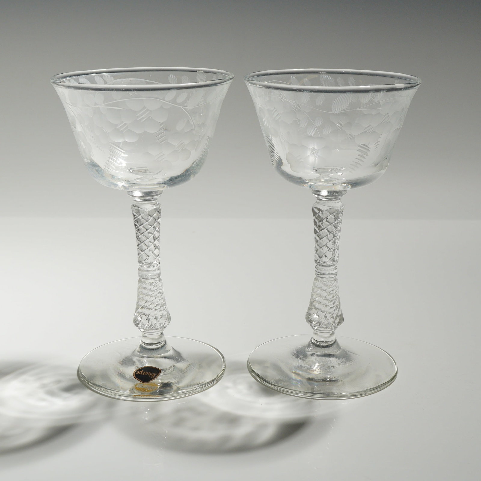 Pair of Rock Sharpe Etched Crystal Champagne Sherbet Glasses: The glasses feature flared bowls decorated with delicate wheel-etched floral and vine motifs. Each bowl is supported by a distinctive twisted texture stem and ends in plain circular feet with smooth, 