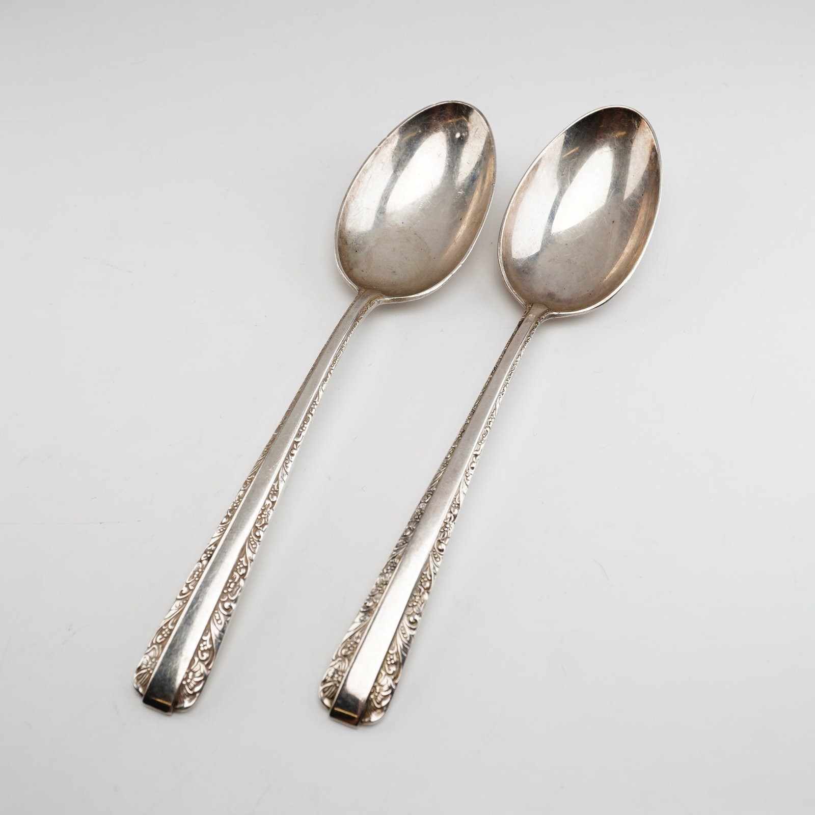 2pc Towle Candlelight Sterling Silver Spoons: Two sterling silver spoons produced by Towle Silversmiths in the Candlelight pattern, which was first introduced in 1934. The handle design features a traditional aesthetic with a border of intricate 