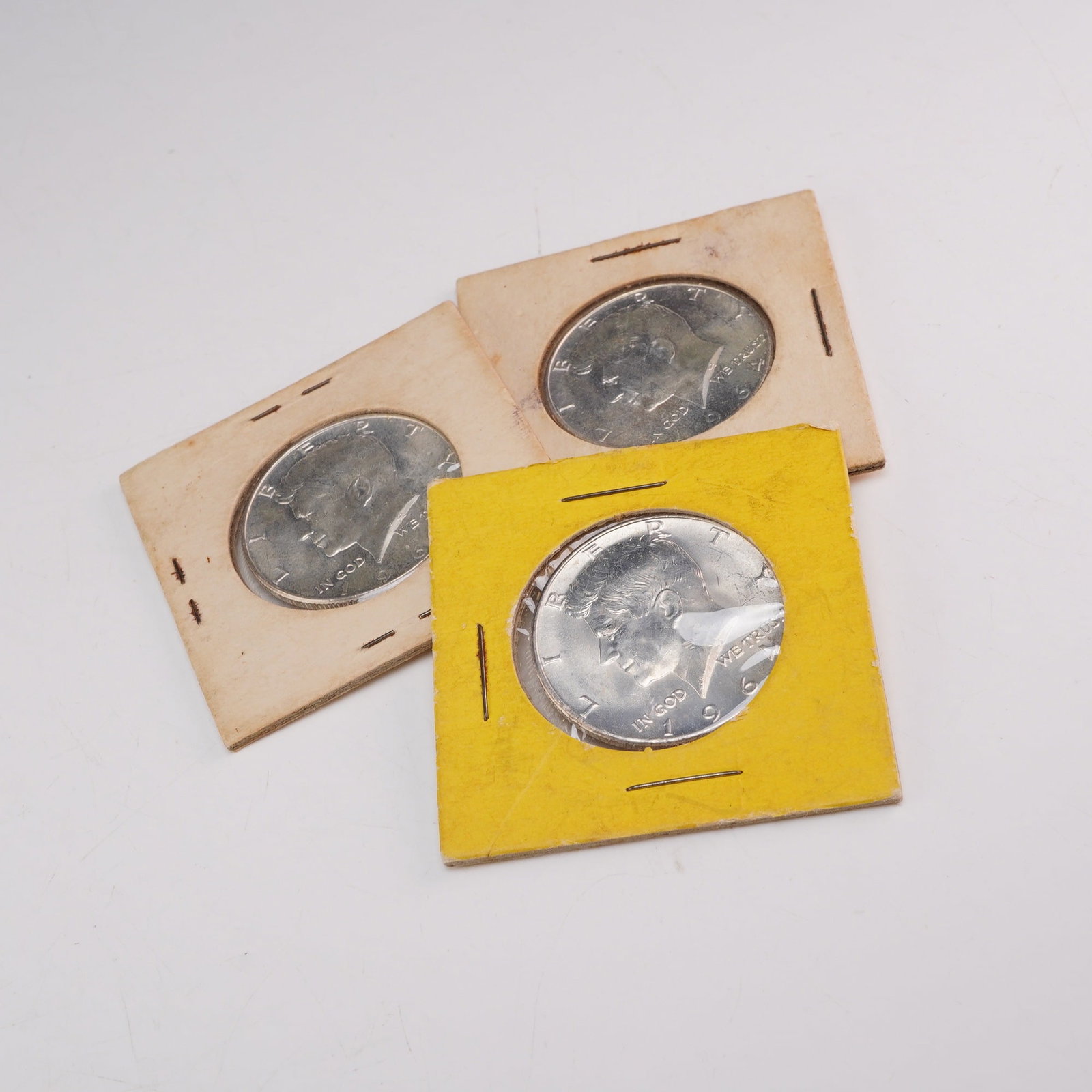 Three 1964 US Kennedy Silver Half Dollars in 2x2 Holders: This lot consists of three US Kennedy half dollars, each dated 1964. These coins are composed of 90% silver and 10% copper. The obverse features the John F. Kennedy portrait, while the reverse display