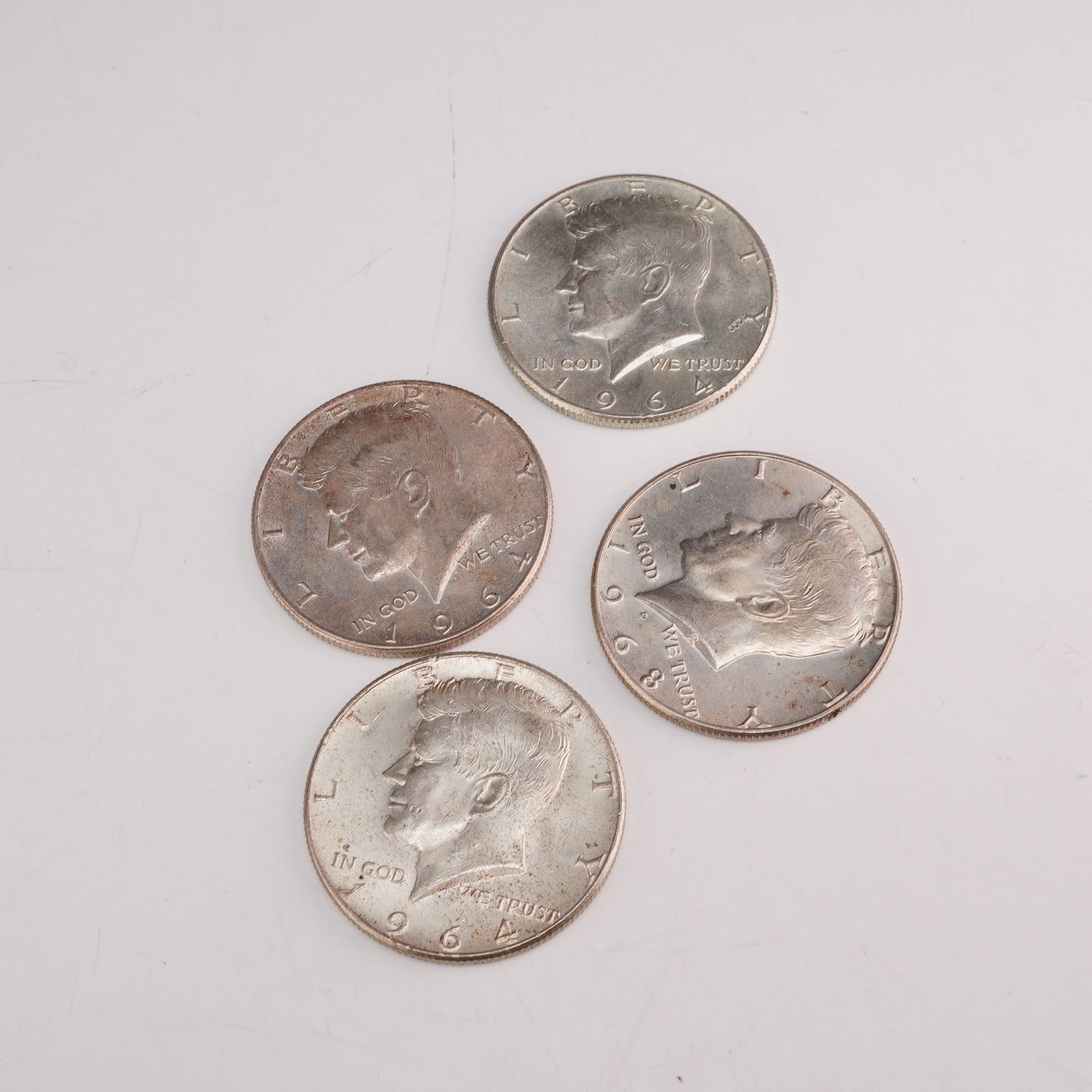 Four 1964 US Kennedy Half-Dollars: A set of four 1964 US Kennedy half-dollars. These coins are struck in 90% silver and 10% copper composition. The obverse design features the profile portrait of John F. Kennedy with the inscriptions L