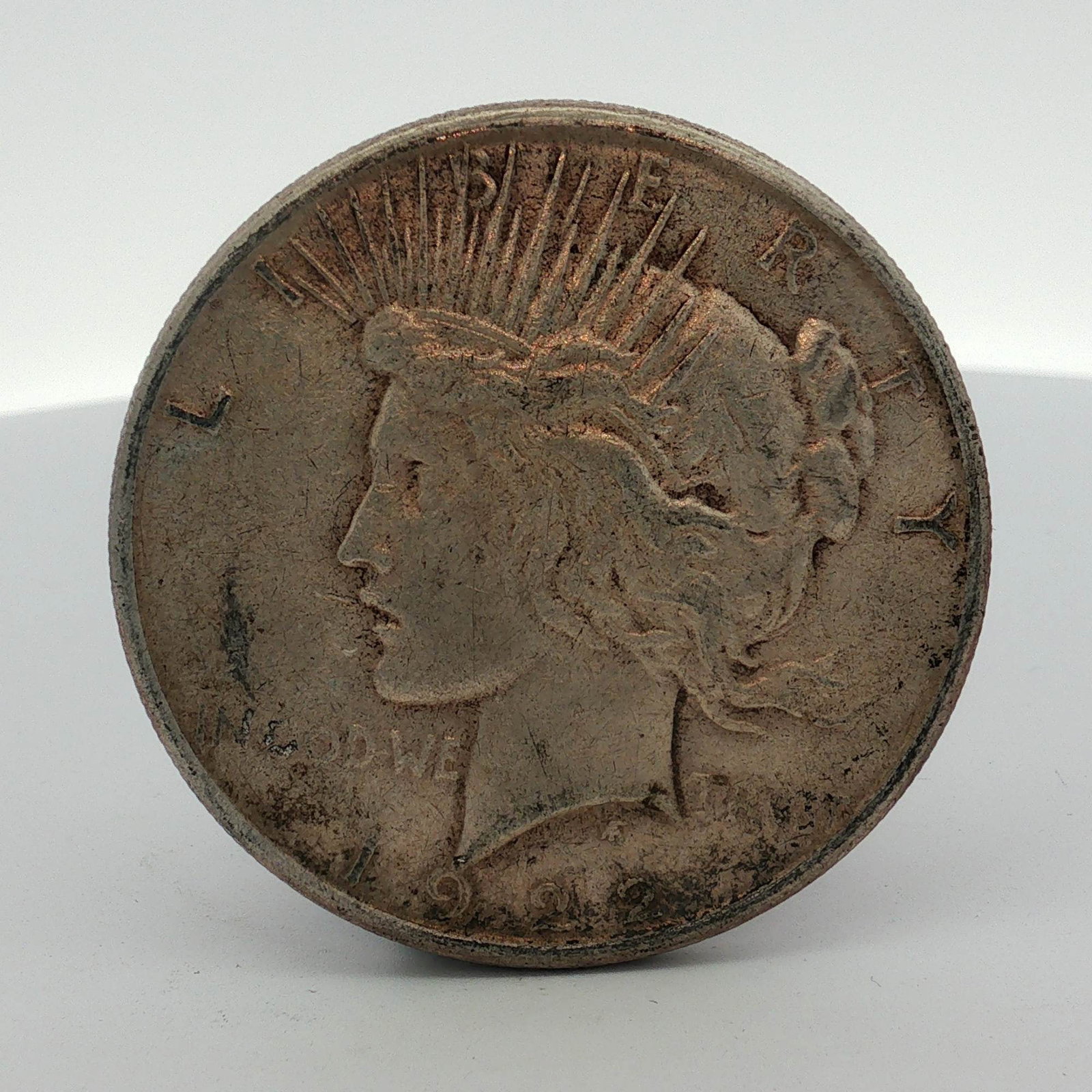 US 1922 Peace Silver Dollar, Philadelphia Mint: This US Peace dollar is a 1922 silver-composition coin struck at the Philadelphia Mint. The coin features the standard radiate head Liberty obverse and eagle on rock reverse. Obverse legends include