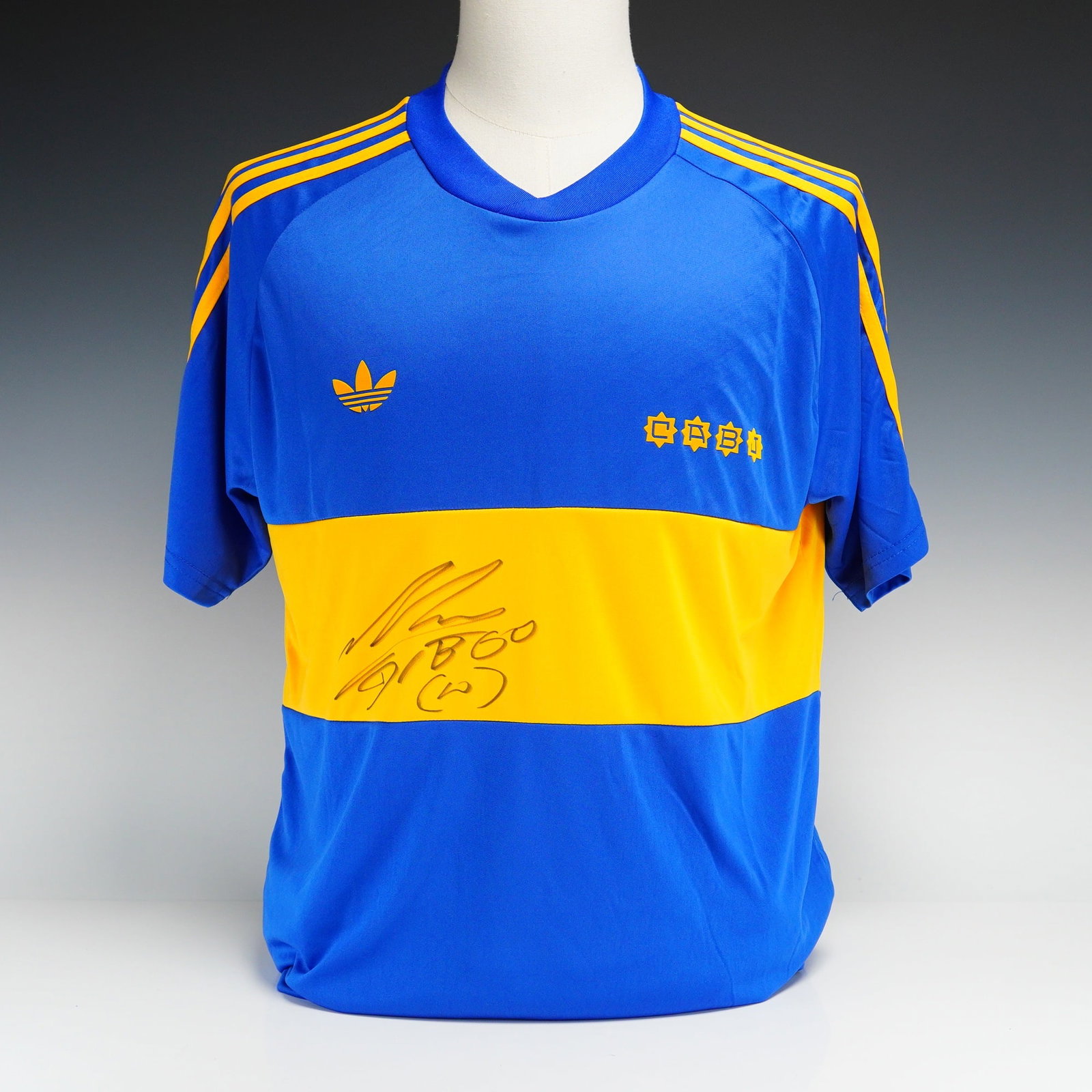 Diego Maradona Signed Boca Juniors 1981-82 Home Shirt with Icons COA: This Boca Juniors home jersey is a reproduction of the 1981-82 season kit, hand-signed by Diego Maradona. The garment is constructed from blue fabric with a wide yellow horizontal band across the