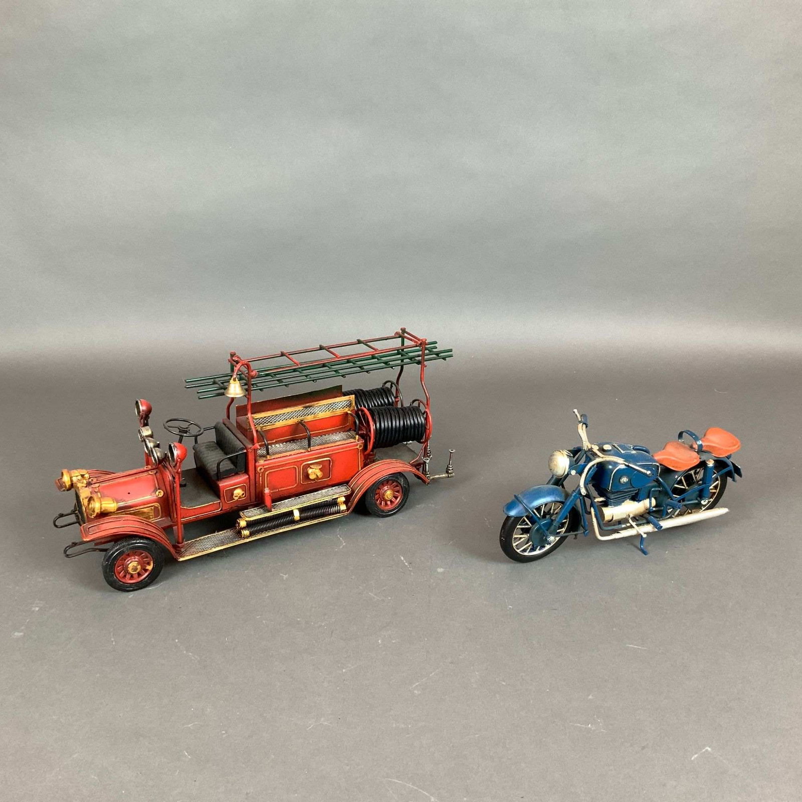 2pc Metal Firetruck and Motorcycle Model Cars: Two modern decorative metal vehicle models designed in a vintage style, comprising a fireman car and a motorcycle. The fire engine model is constructed from painted tin with a red body, gold-tone