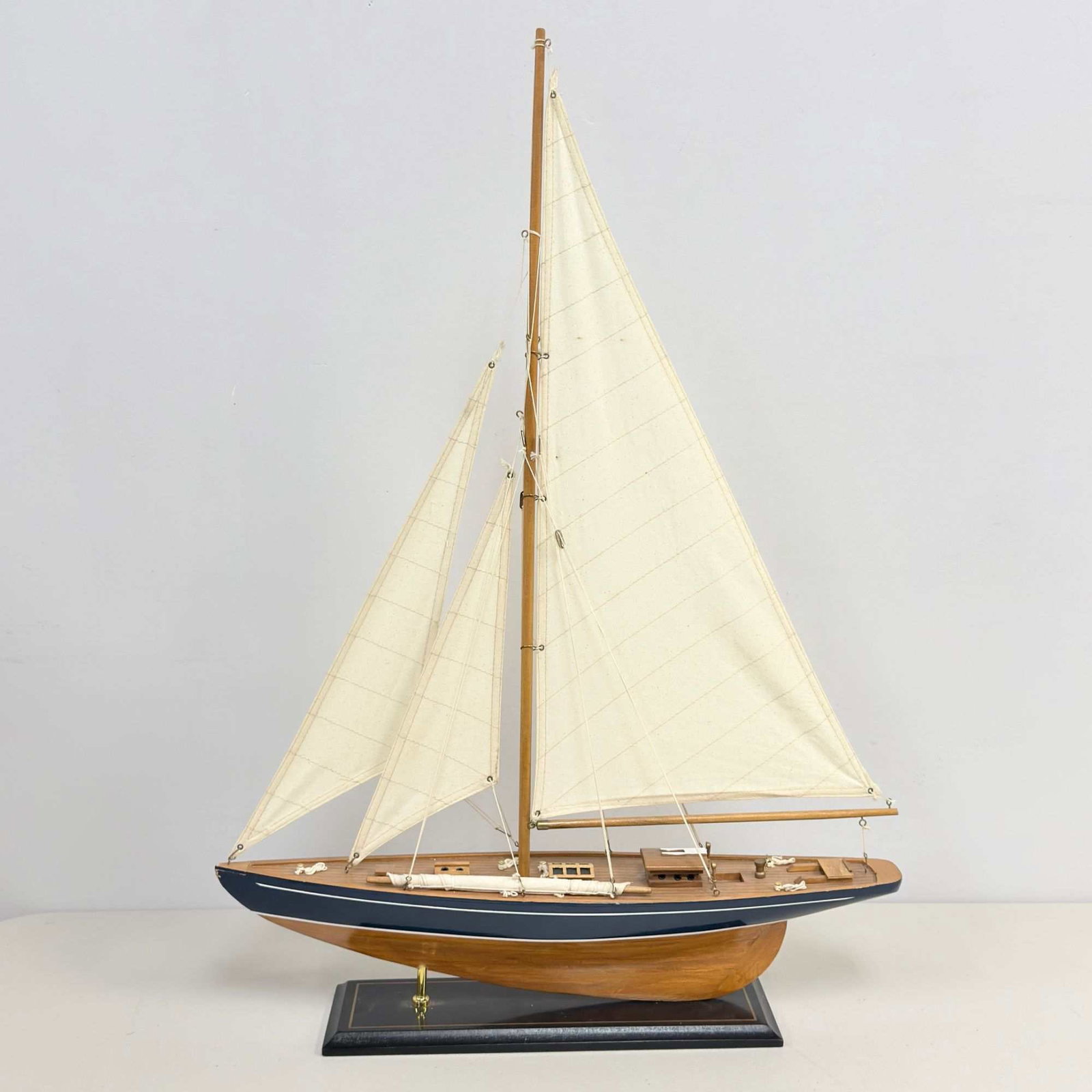 Classic Handcrafted Sailboat Model Yacht: A contemporary decorative classic sailboat handcrafted model yacht, styled after a racing sloop or pond yacht. The vessel features a wooden hull with a deep blue painted topside accented by a thin