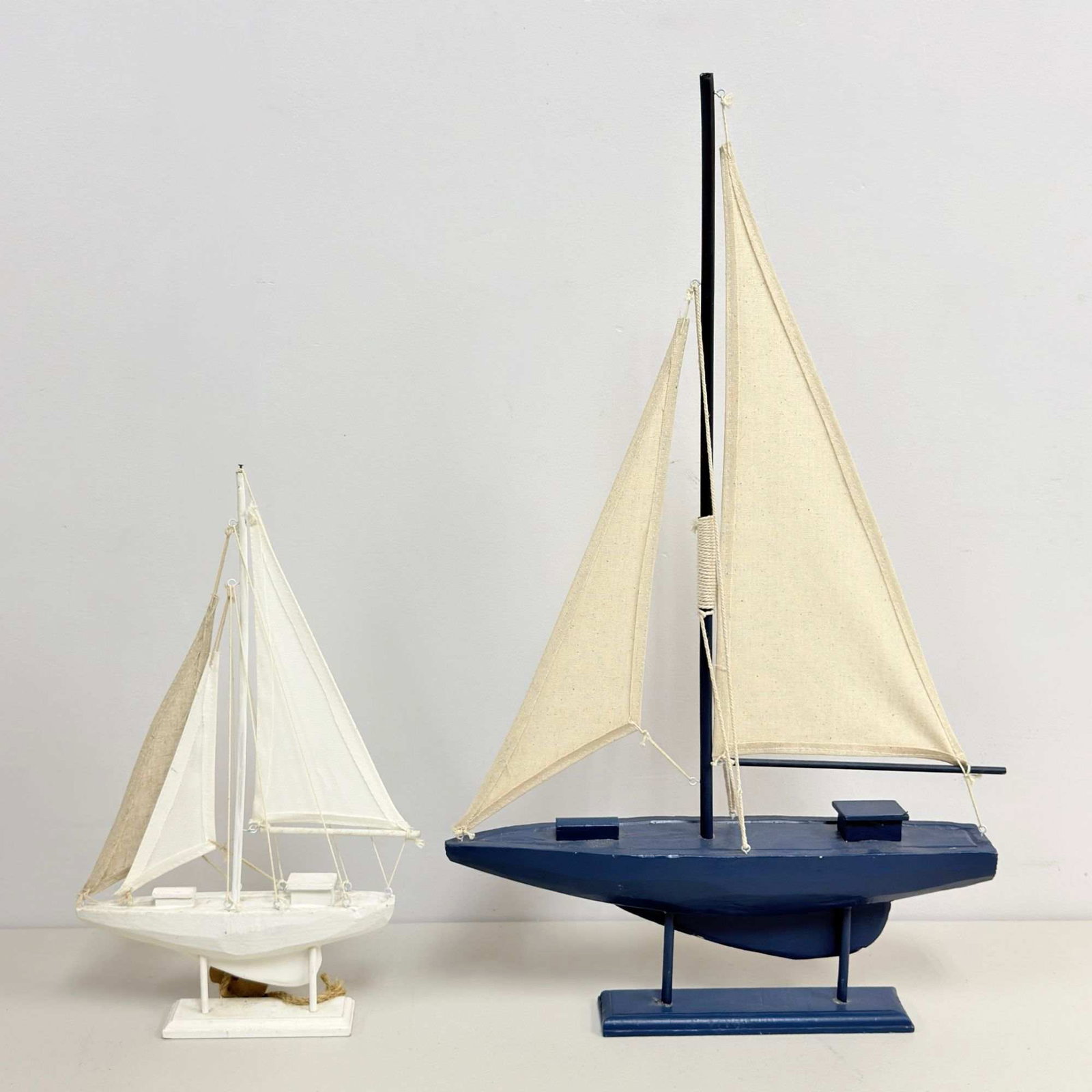 2 Wooden Sailing Boats Decorative Models: A group of contemporary decorative wooden sailing boat models designed for interior display. These vessels are constructed with carved and painted wooden hulls and bases, featuring fabric sails and