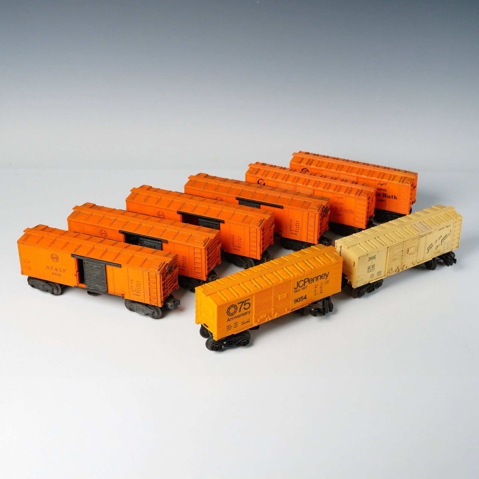 8pc Lionel O Gauge Model Railroad Boxcars: The cars are constructed primarily from molded plastic with metal components used for the trucks and couplers. The set includes eight cars finished in bright orange, predominantly featuring the Atchis