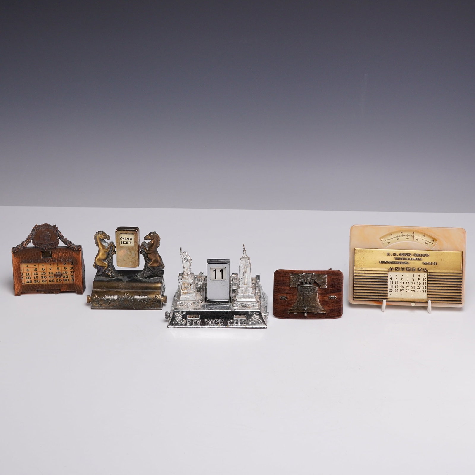 Lot of 5 Collectibles Including Four Perpetual Calendars and One Bicentennial Belt Buckle: This lot consists of 5 collectibles including four calendars and one belt buckle. The collection features a variety of mid-20th century desk accessories and commemorative items. The first item is an o