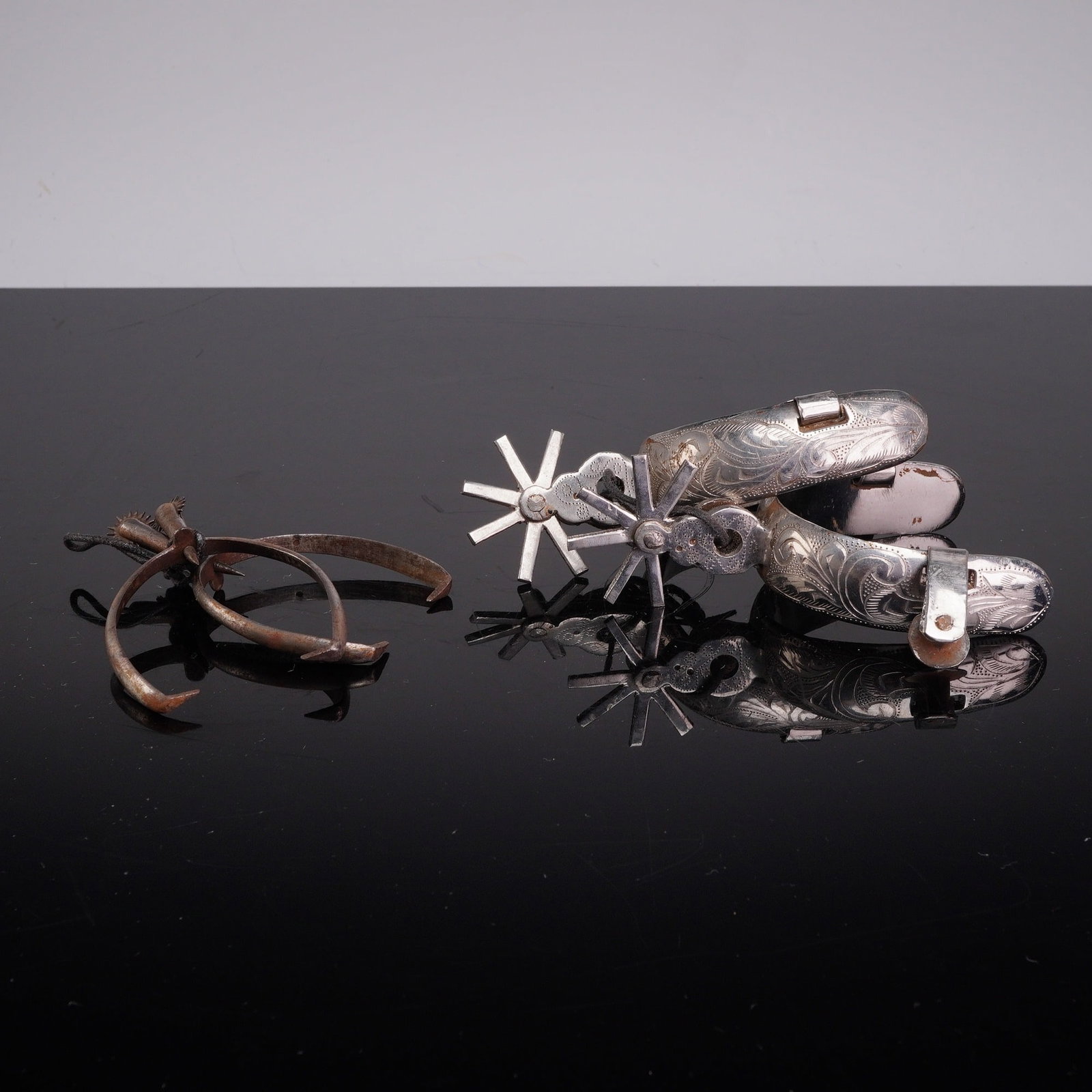 Two Pairs of Mexican Charro Style Metal Spurs: This lot features two pairs of metal spurs, following the identification provided in the user facts. The primary pair is consistent with Mexican Charro style steel spurs, featuring wide heel bands