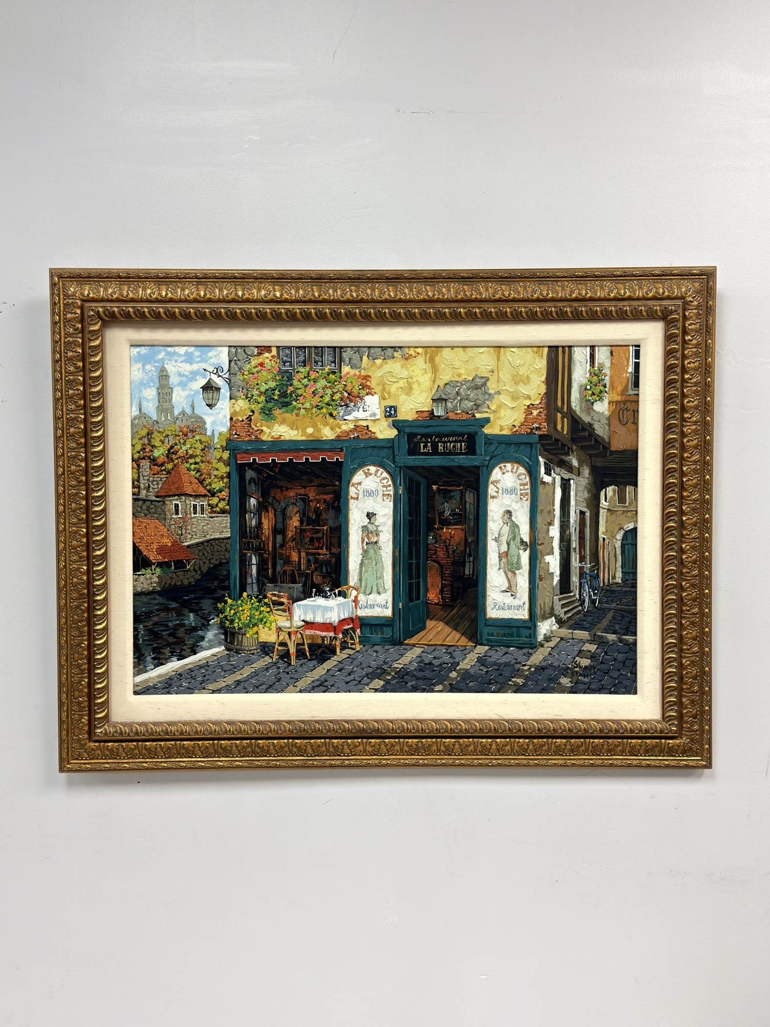 Viktor Shvaiko (Russian, b. 1965) Hand Embellished Serigraph on Canvas, Castle by the Water: This hand-embellished serigraph on canvas is titled Castle by the Water. The work depicts a quaint European street scene featuring a restaurant storefront titled La Ruche, complete with an outdoor