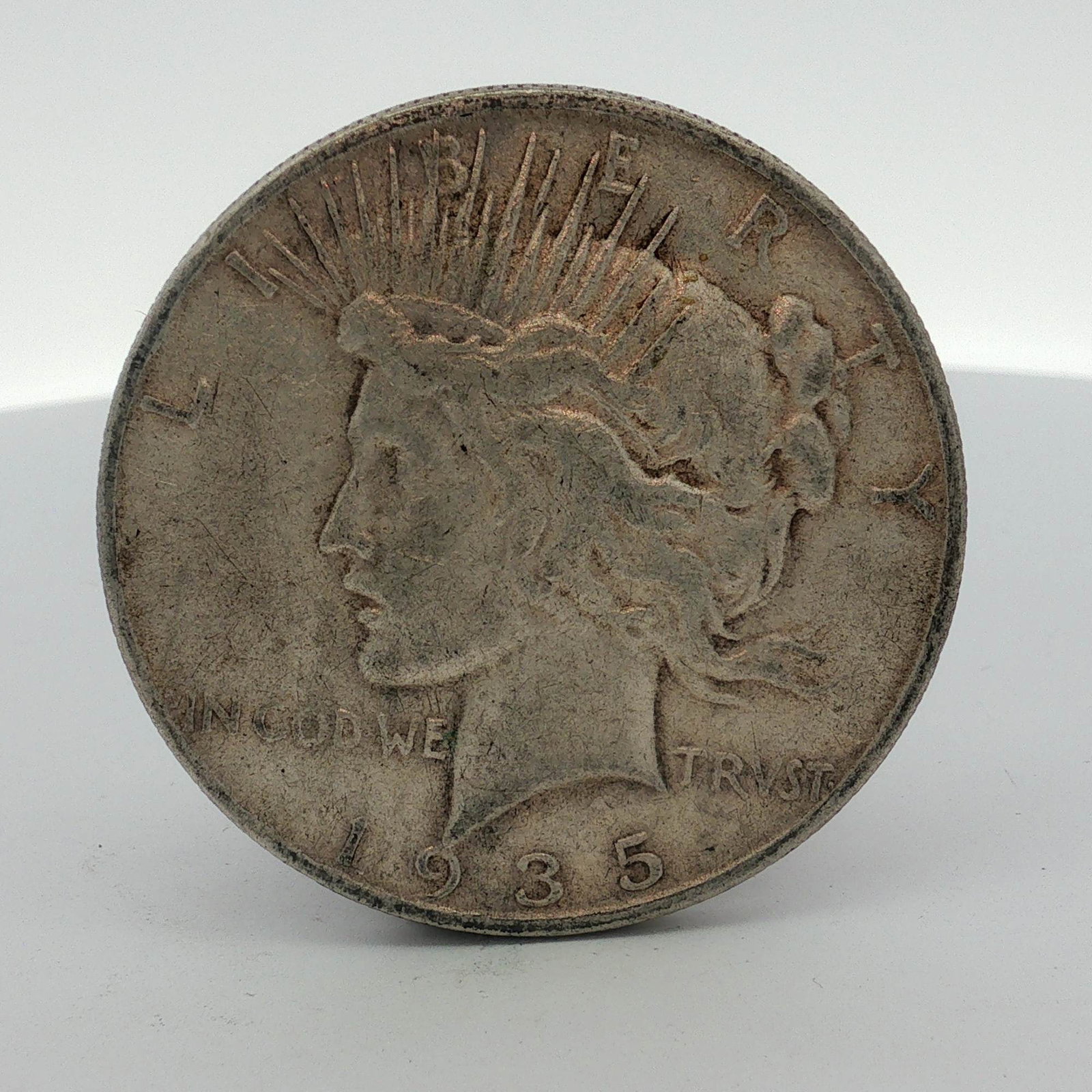 1935-S US Peace Silver Dollar: This is a 1935-S US Peace silver dollar, a struck coin composed of 0.900 fine silver and 0.100 copper. The obverse features the standard Liberty head design with a radiate crown as created by Anthony