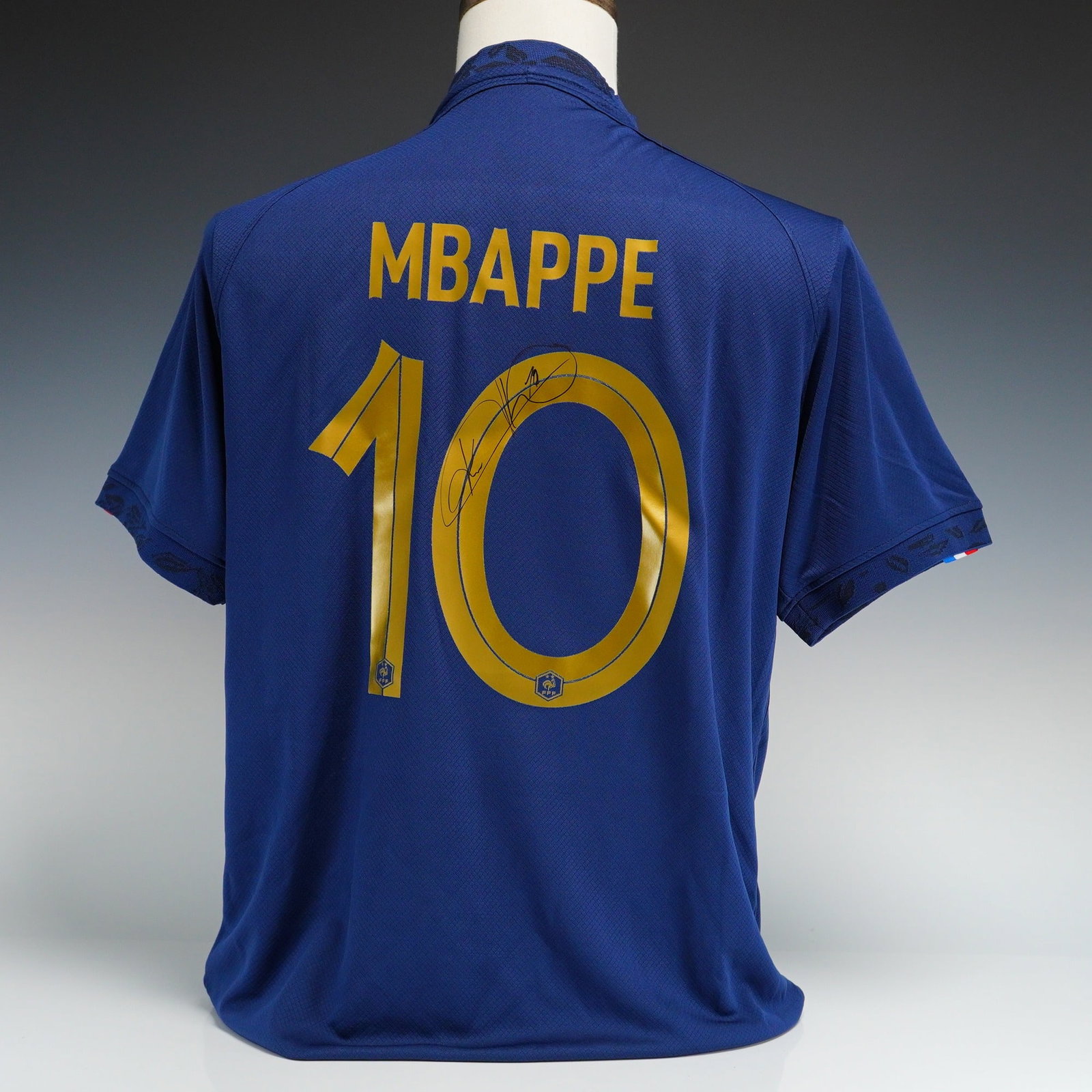 Kylian Mbappe Autographed 2022-23 France National Team Home Jersey Size with COA: This is a France National Team 2022-23 home soccer jersey manufactured by Nike, signed by forward Kylian Mbappe. The jersey is a men size XL replica shirt in navy blue with gold-tone accents. The fron