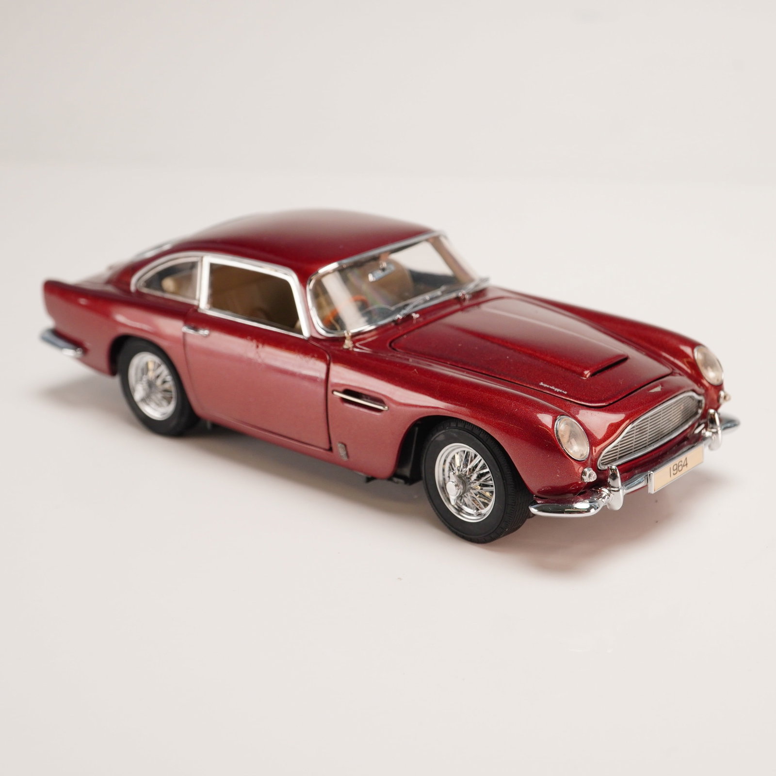 The Danbury Mint Classic Model Car, 1964 Aston Martin DB5: This 1:24 scale die-cast model vehicle is a replica of a 1964 Aston Martin DB5 Coupe, produced by The Danbury Mint as part of their Classic Cars collection. The model features a Dubonnet Red exterior