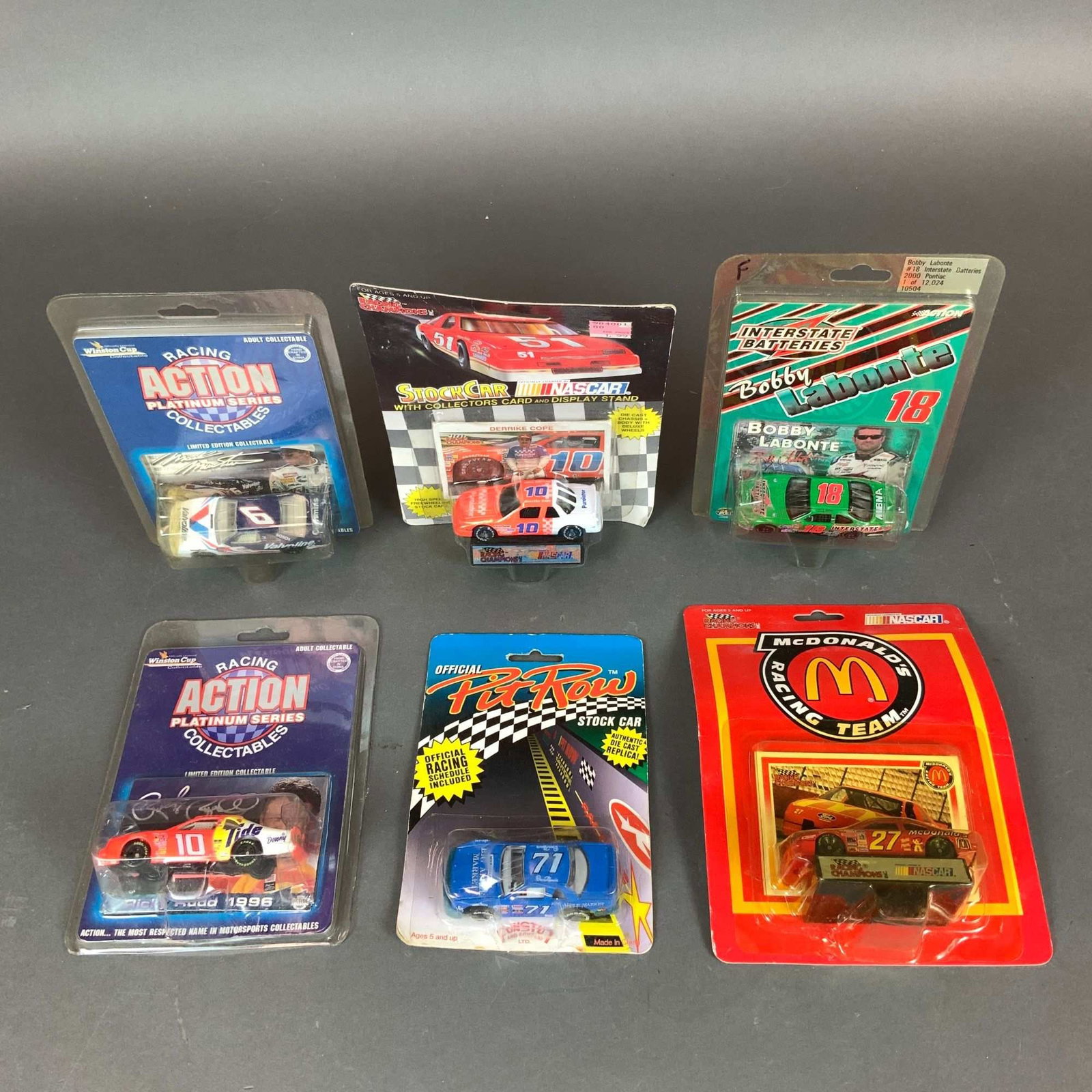 6pc Lot of 1:64 Scale NASCAR Collectible Die-Cast Model Cars: A collection of six vintage NASCAR die-cast model cars in 1:64 scale, each housed in its original blister pack. The assortment includes vehicles from various manufacturers and series prominent in the