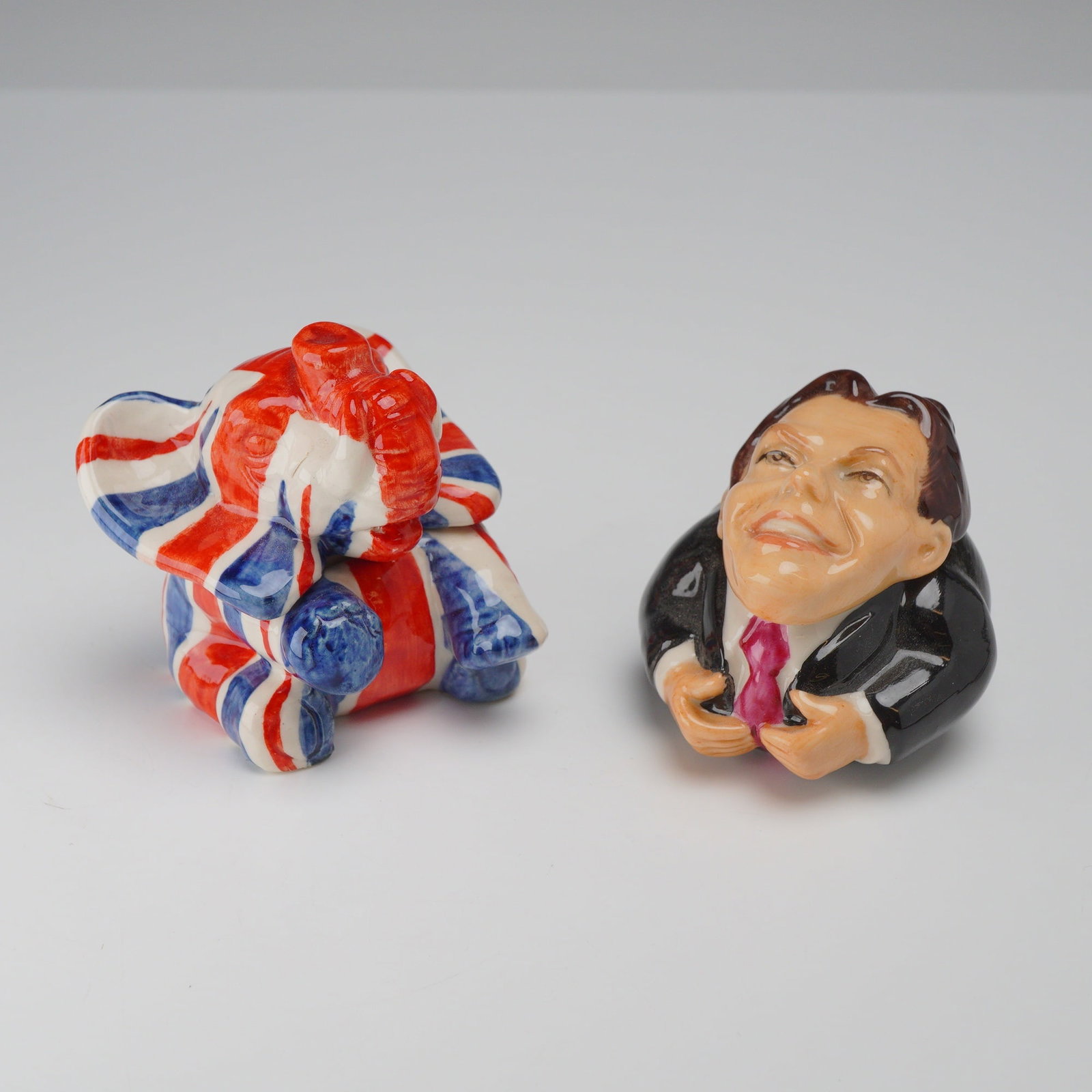 2pc Kevin Francis Ceramic Face Pots, British Theme: A pair of hand-painted polychrome glazed ceramic lidded miniature boxes, known as Face Pots, produced by Kevin Francis. This collection features two distinct designs centered on a British theme. The