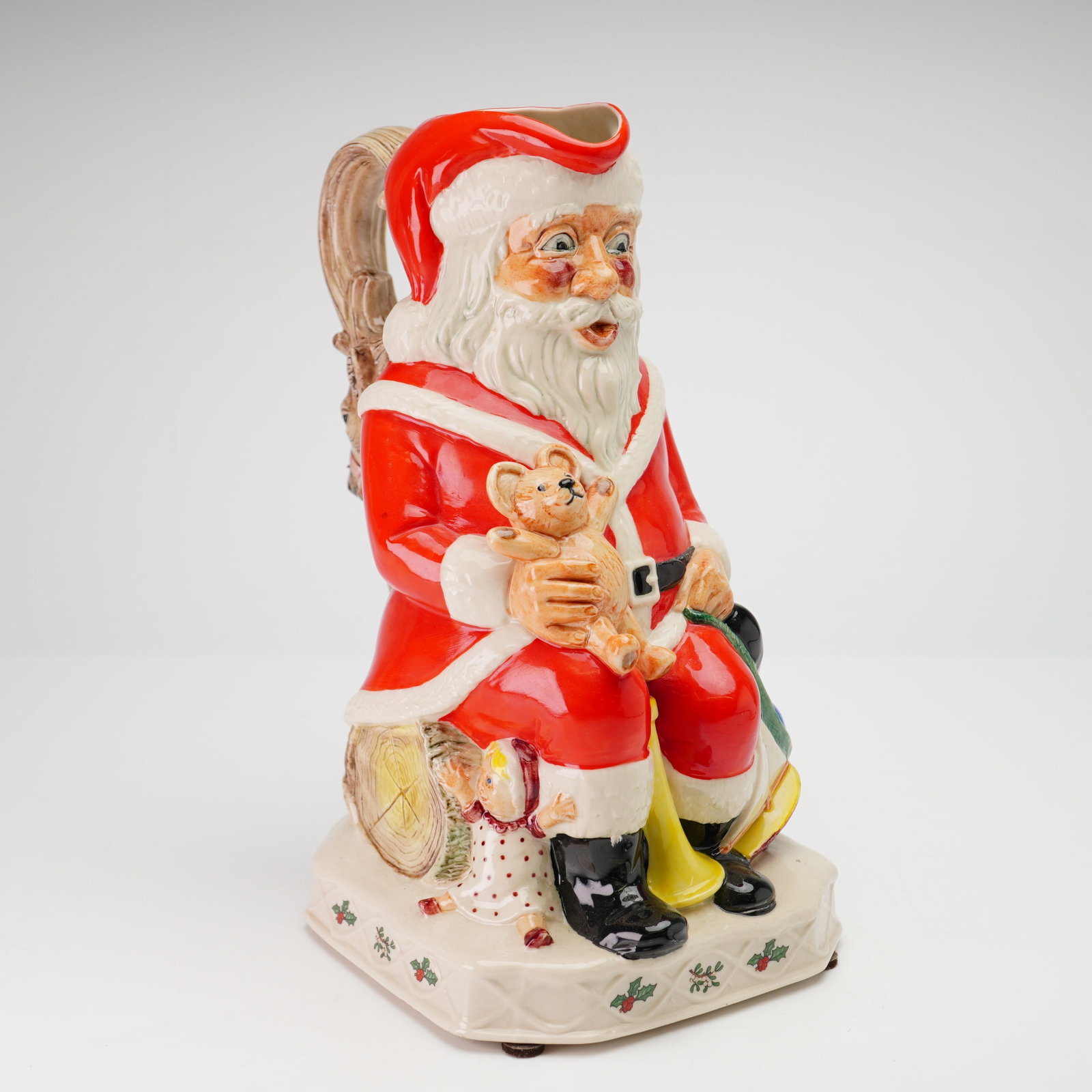 Kevin Francis Ceramics Limited Edition Toby Jug, Santa Claus: It depicts a seated Santa Claus in a traditional red and white suit, resting on a naturalistic log base. Santa holds a small teddy bear in his lap, while a small child or doll is positioned at his fee