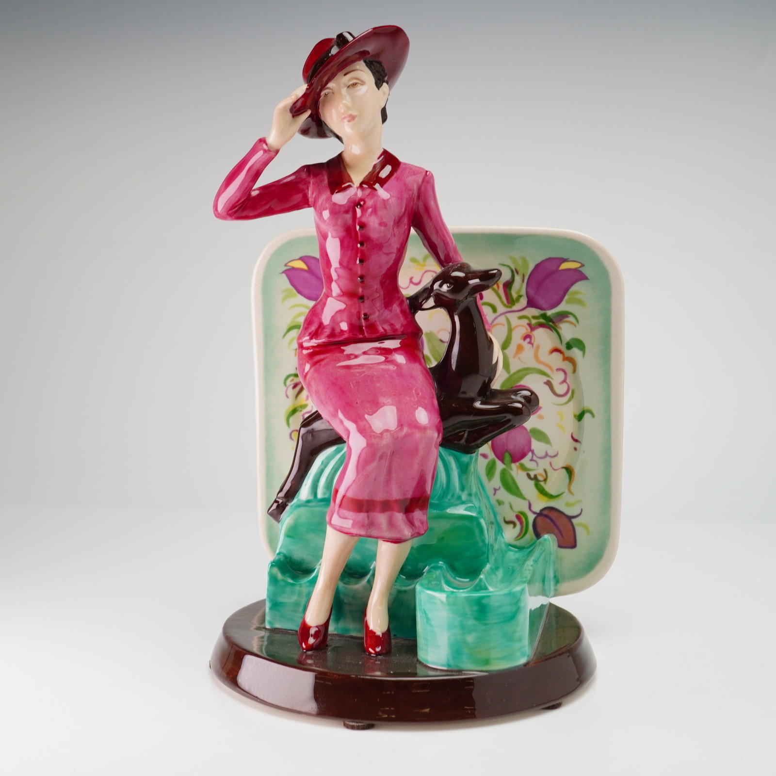 Kevin Francis Ceramics Limited Edition Porcelain Figurine, Susie Cooper: This piece serves as a tribute to the celebrated ceramic designer, depicting her in stylized 1930s-era attire. The figure wears a wide-brimmed magenta hat, a matching button-down jacket and skirt, and