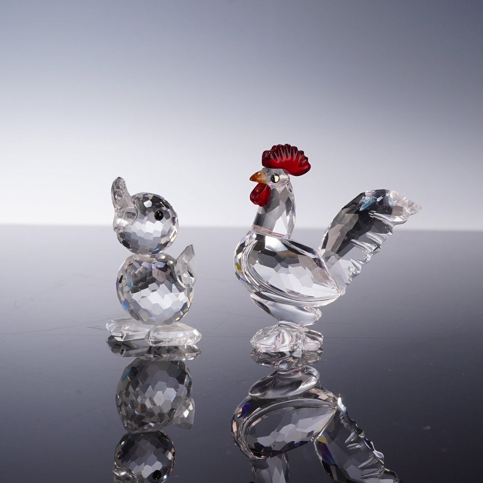 2pc Swarovski Crystal Figurines, Cockerel and Drake Mini: This lot contains two Swarovski lead crystal figurines representing a cockerel and a duck. The cockerel is designed with a faceted clear crystal body, a red crystal comb and wattle, an amber-hued beak