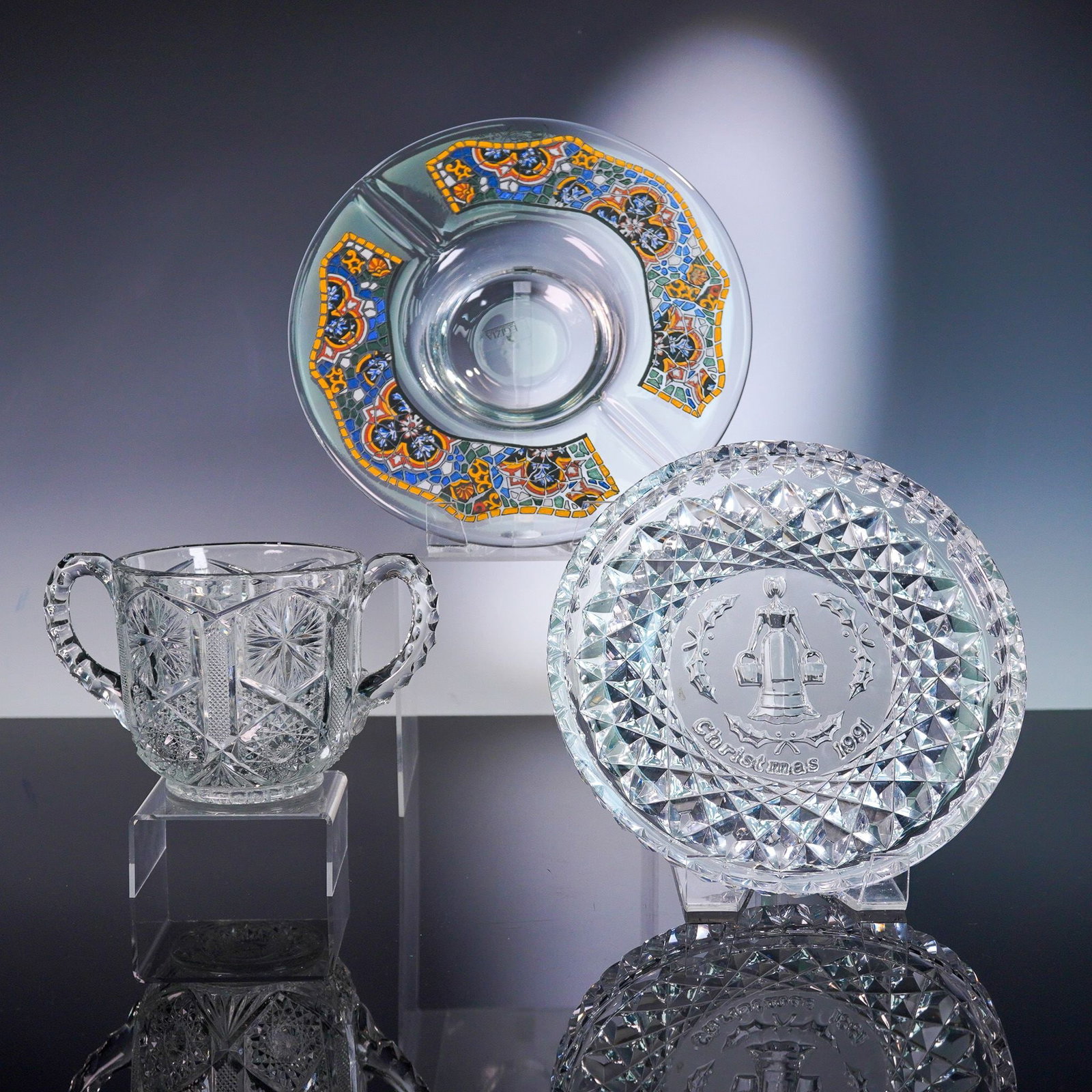 3pc Glass Serveware Lot: This lot comprises a cut-glass handled sugar bowl with double-drop handles and crisp starburst and hobnail cuts; a decorative mosaic glass charger plate featuring a vibrant enamel tessellated pattern 