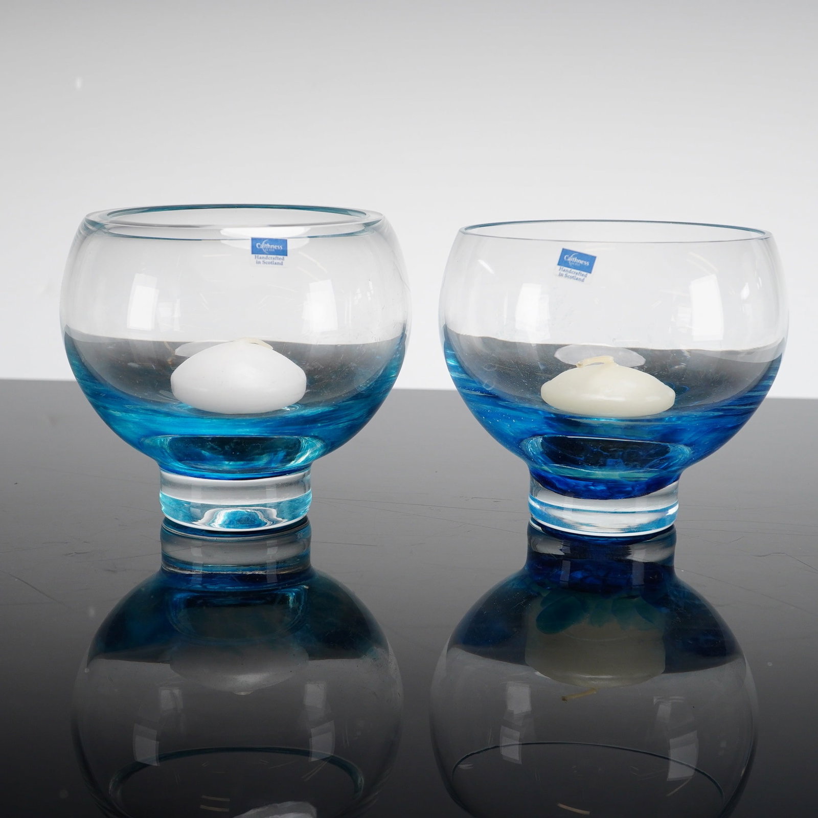 Pair of Caithness Glass Handcrafted Candle Holders: A pair of handcrafted art glass candle holders by Caithness Glass. Each piece features a modern rounded bowl form set upon a thick clear pedestal base. The upper sections are clear glass, while the