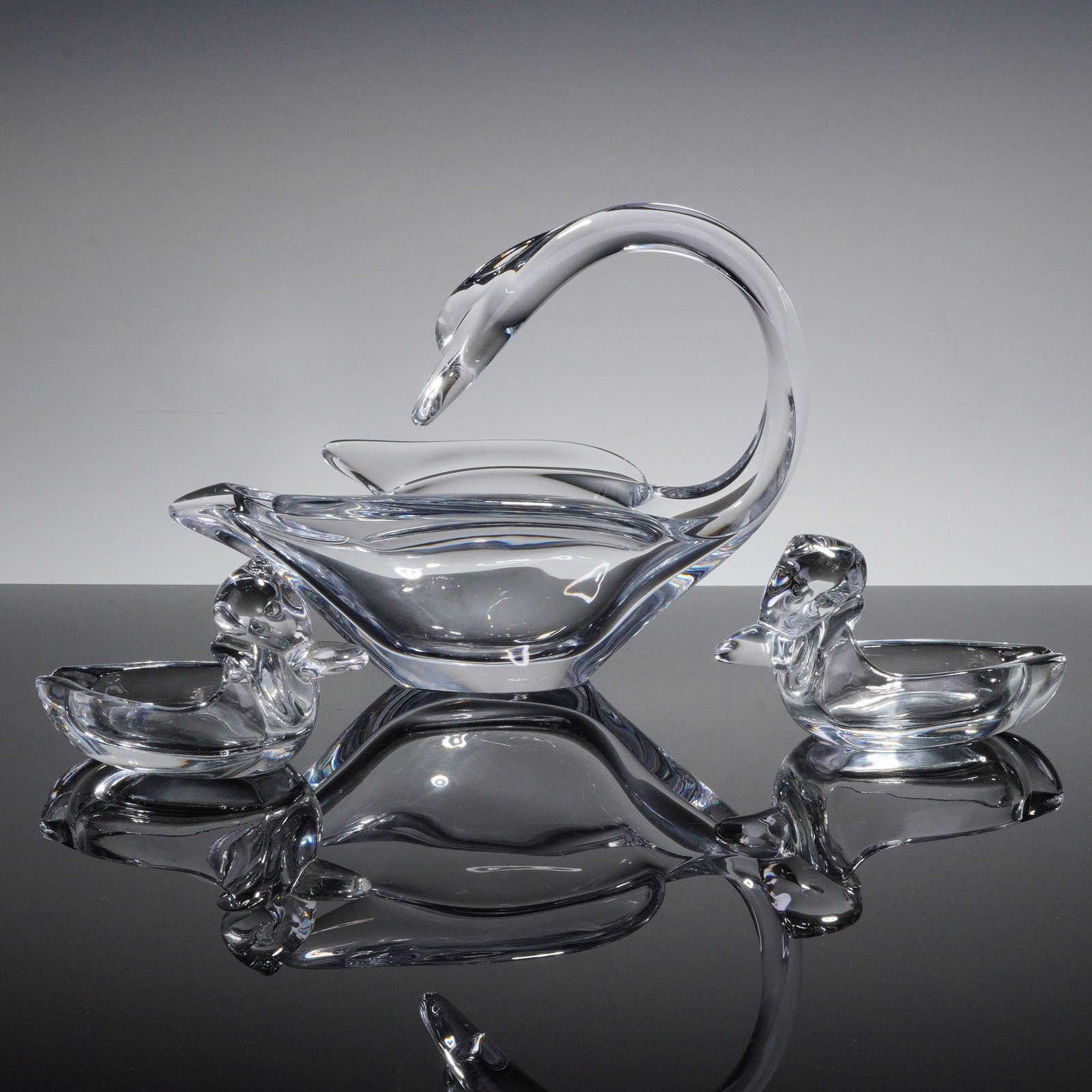 A Three-Piece Vannes-le-Chatel Crystal Swan Dish and Duck Ashtrays Set: A three-piece set of clear, colorless heavy crystal decorative tableware attributed to Vannes-le-Chatel, France. The collection comprises one large centerpiece bowl stylized as a swan with an