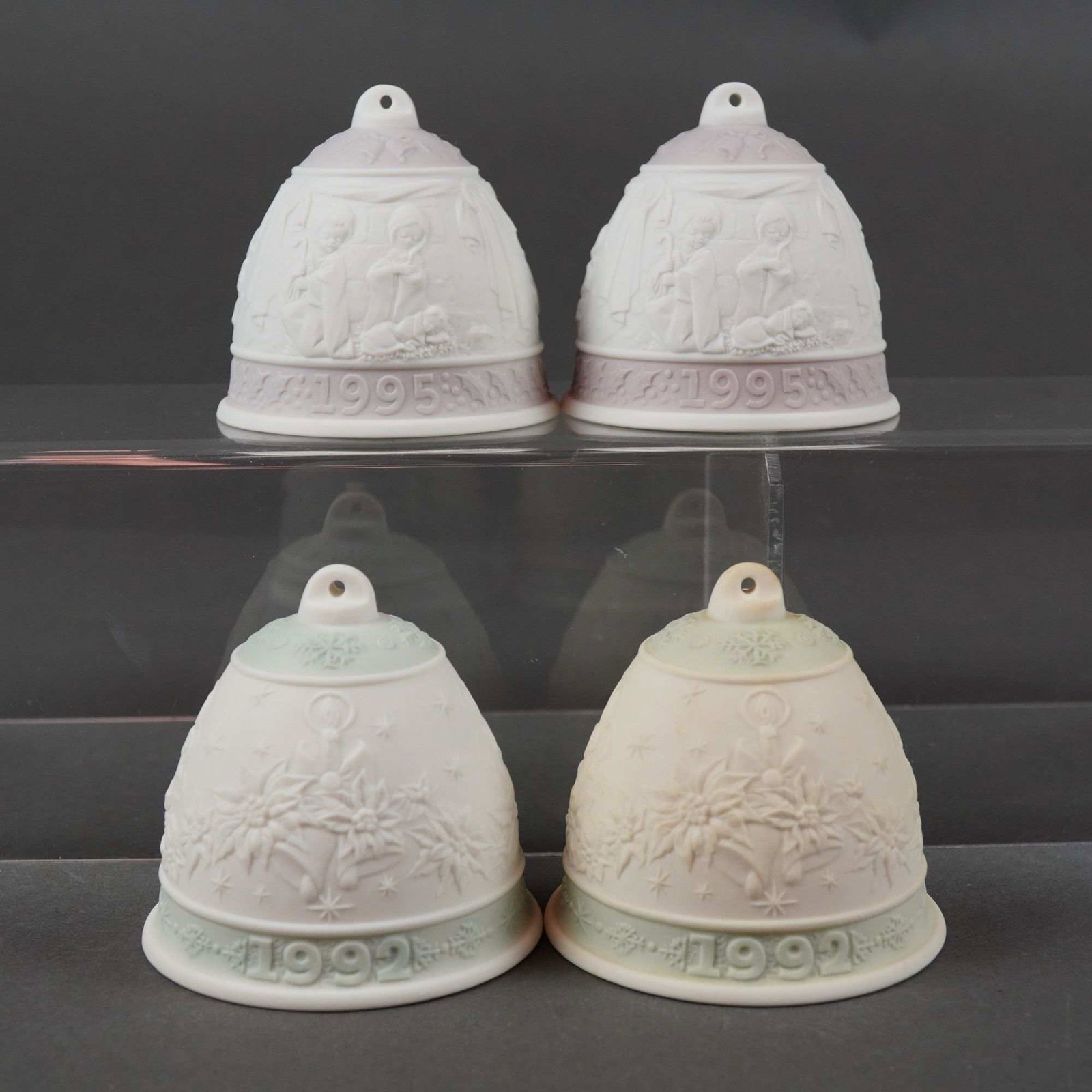Lladro Annual Christmas Bells: This 4pc Lladro bell grouping consists of two matching pairs of annual ornaments from 1992 and 1995. Crafted in fine matte bisque porcelain, the 1992 bells feature a low-relief design of poinsettia fl