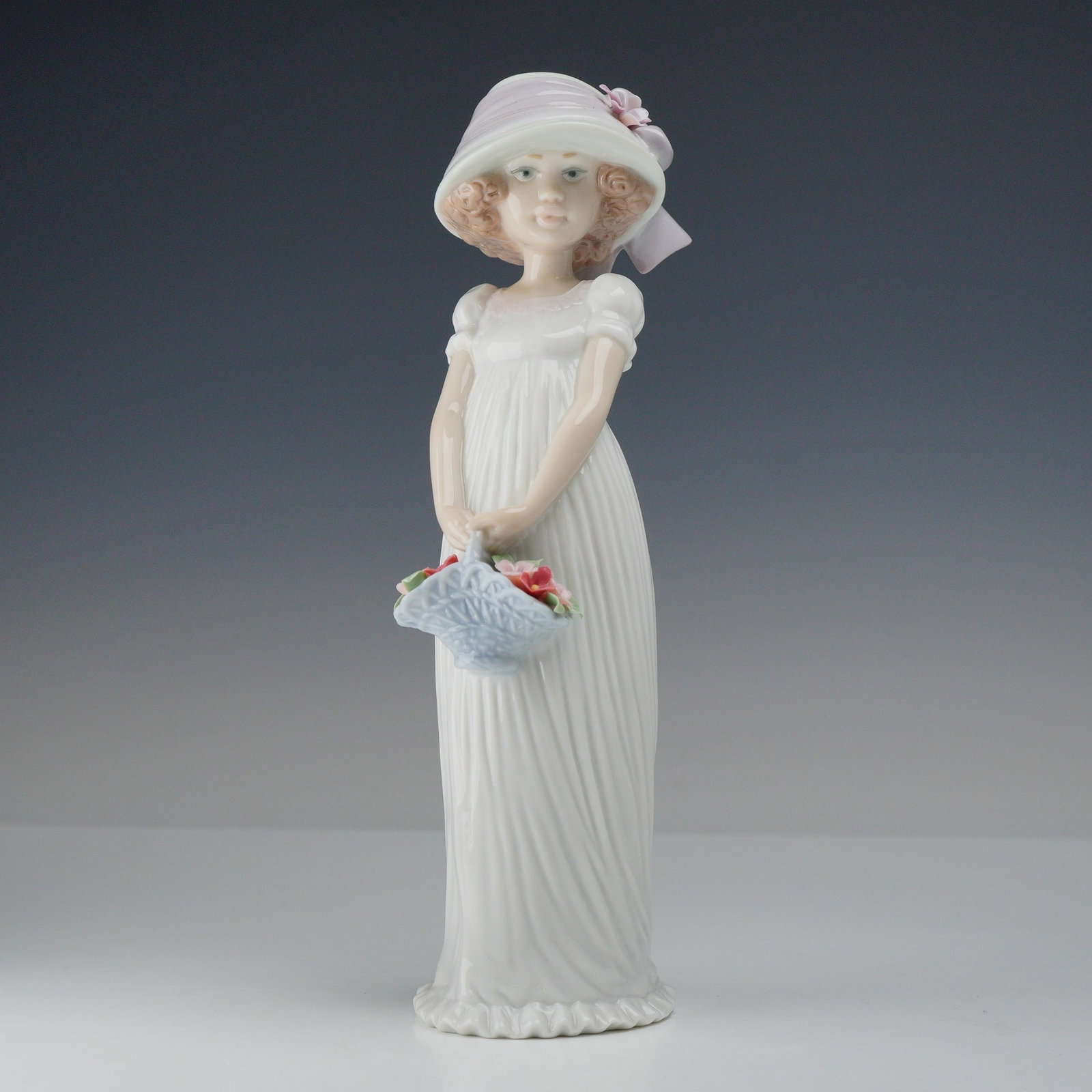 Lladro Porcelain Figurine Little Lady 01008022: This Lladro glazed porcelain figurine depicts a young woman in a classic Romantic-style pose. She is dressed in a long, high-waisted white gown featuring fine vertical pleating and short puffed sleeve