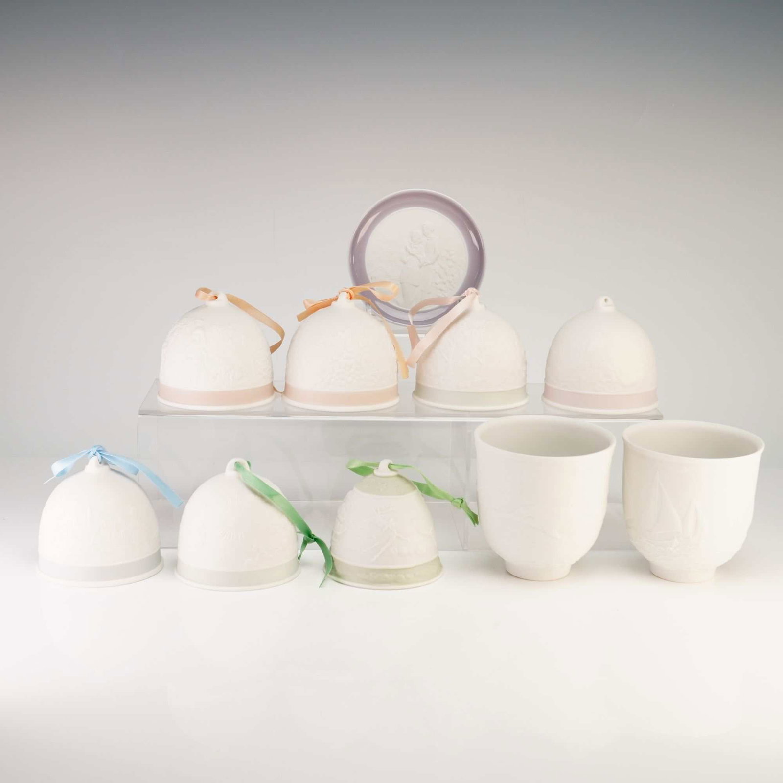 Collection of Ten Lladro Collectors Society Bisque Porcelain- Bells, Cups and Dish: This collection includes ten items produced by Lladro for the Collectors Society, featuring matte bisque porcelain with detailed bas-relief decoration. The set is comprised of seven holiday bell ornam