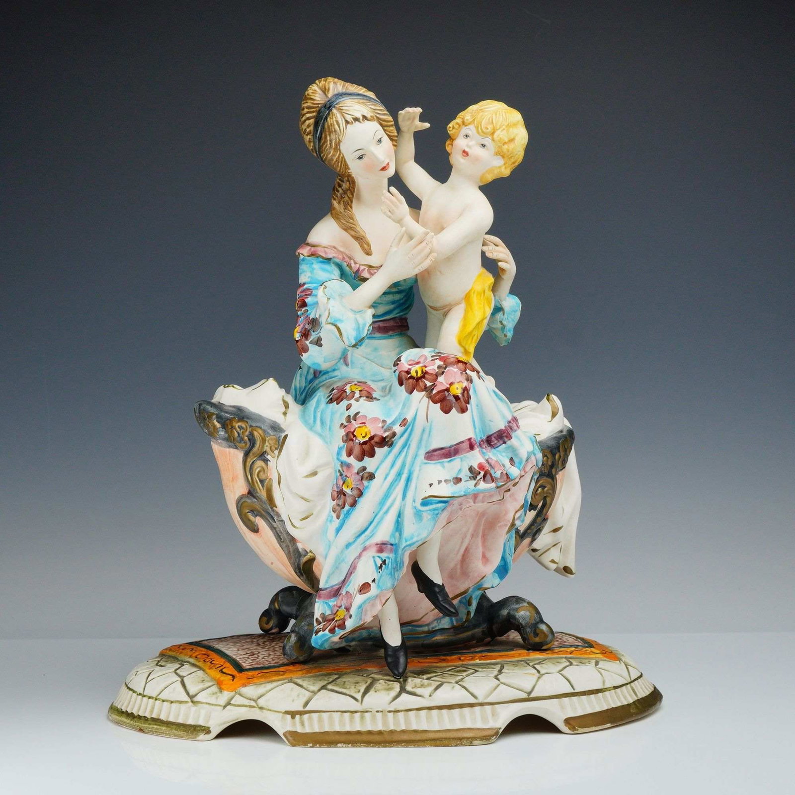 Capodimonte Made in Italy Hand-Painted Porcelain Mother and Child Figurine: This hand-painted porcelain figure produced in the Capodimonte tradition depicts a mother and child in a Rococo-revival style. The seated woman is dressed in an 18th-century style blue gown decorated 