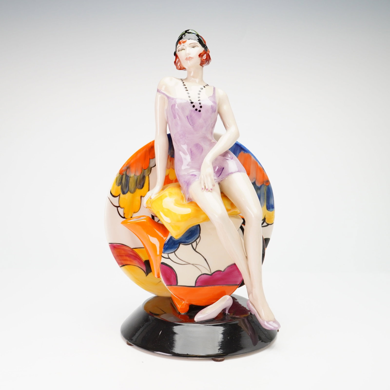 Peggy Davies Limited Edition Ceramic Figurine, Nostalgia: This hand-painted ceramic figurine modeled by Andy Moss, the piece depicts a woman in 1920s-style attire featuring a lilac slip dress, a black beaded necklace, and a decorative headband. She is seated