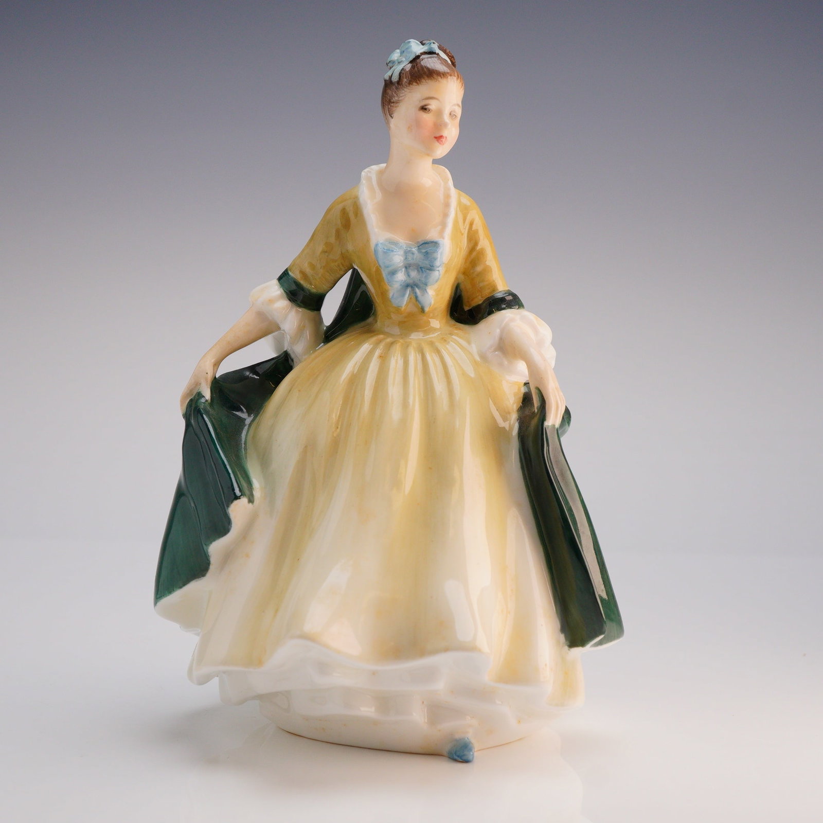 Royal Doulton Figurine Elegance HN 2264: The figure depicts a woman dressed in a historical-style gown, hand-painted in polychrome enamels. The figure is characterized by a pale yellow and cream skirt, an ochre bodice, white cuffs, and a dee