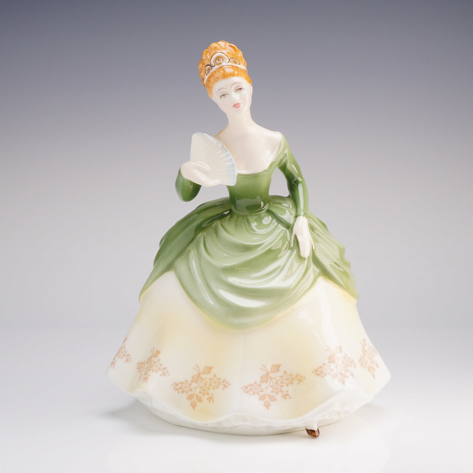 Royal Doulton Figurine Soiree HN2312: The figurine depicts a woman in 18th or 19th-century attire holding a white fan. The polychrome decoration features an olive-green draped overskirt and bodice contrasting with a cream and yellow under