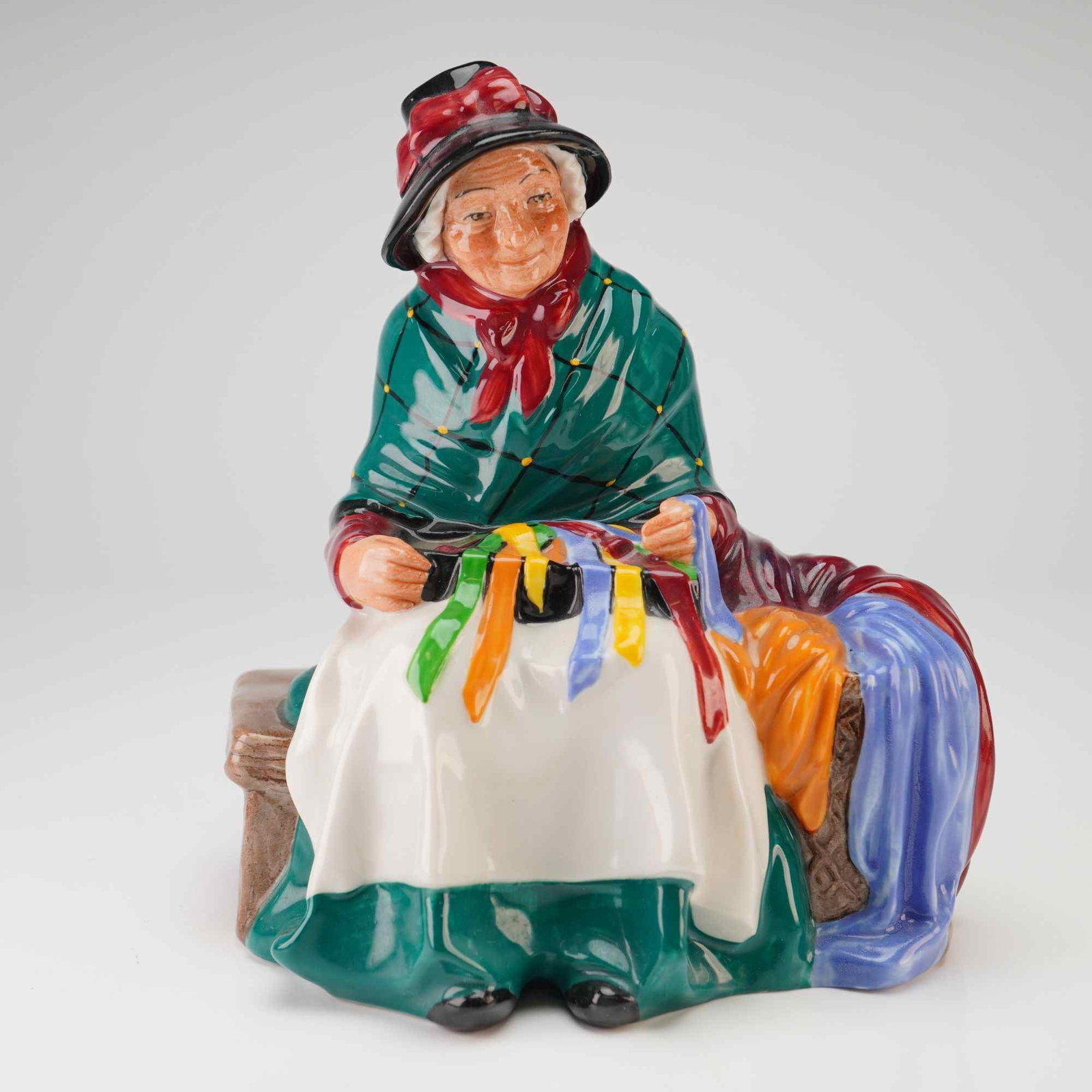 Royal Doulton Figurine, Silks and Ribbons HN2017: A fine Royal Doulton bone china figurine titled Silks and Ribbons, model number HN 2017, originally designed by Leslie Harradine. This hand-painted piece depicts an elderly street vendor seated on a s