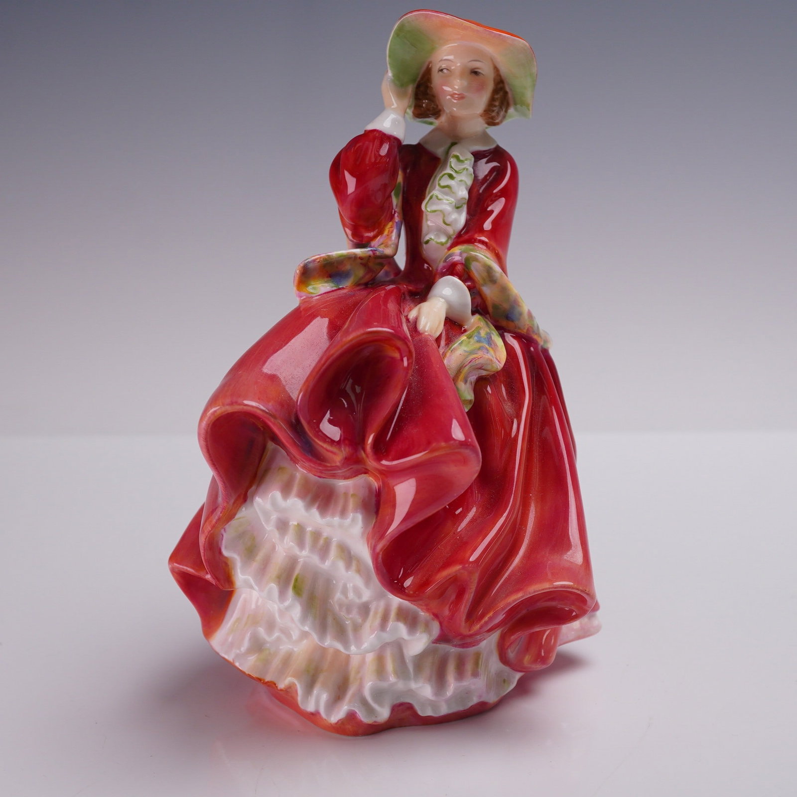 Royal Doulton Figurine, Top o'the Hill HN1834: Bone china figure represents the first version of one of Leslie Harradine's most recognized creations. It features a young woman in a wind-swept pose, grasping her bonnet, dressed in a deep red flowin
