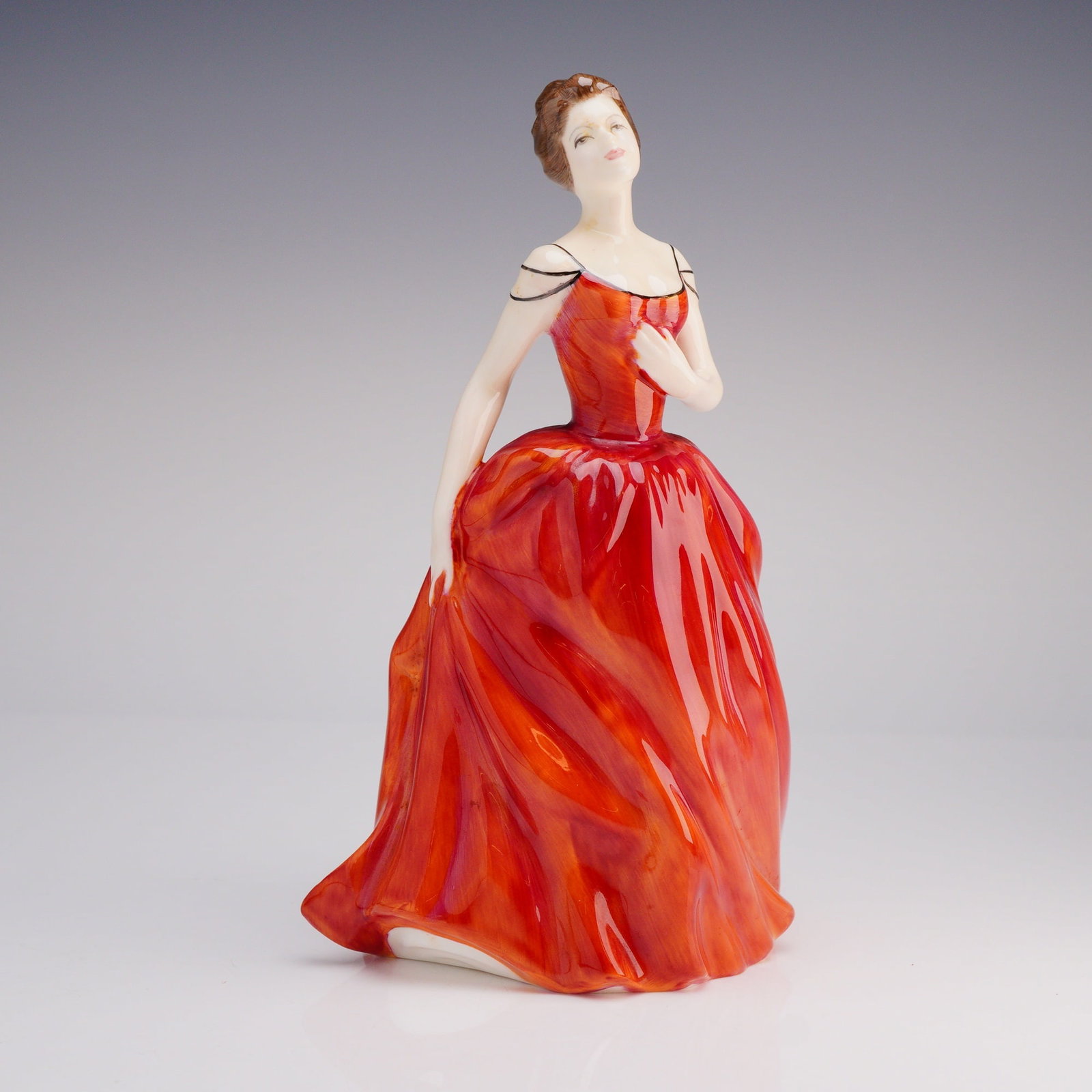 Royal Doulton Innocence HN 2842 Figurine: The figurine depicts a standing woman modeled in a pose suggesting movement, wearing a voluminous, floor-length ballgown glazed in a vibrant, high-gloss red and orange coloration. The figure is marked