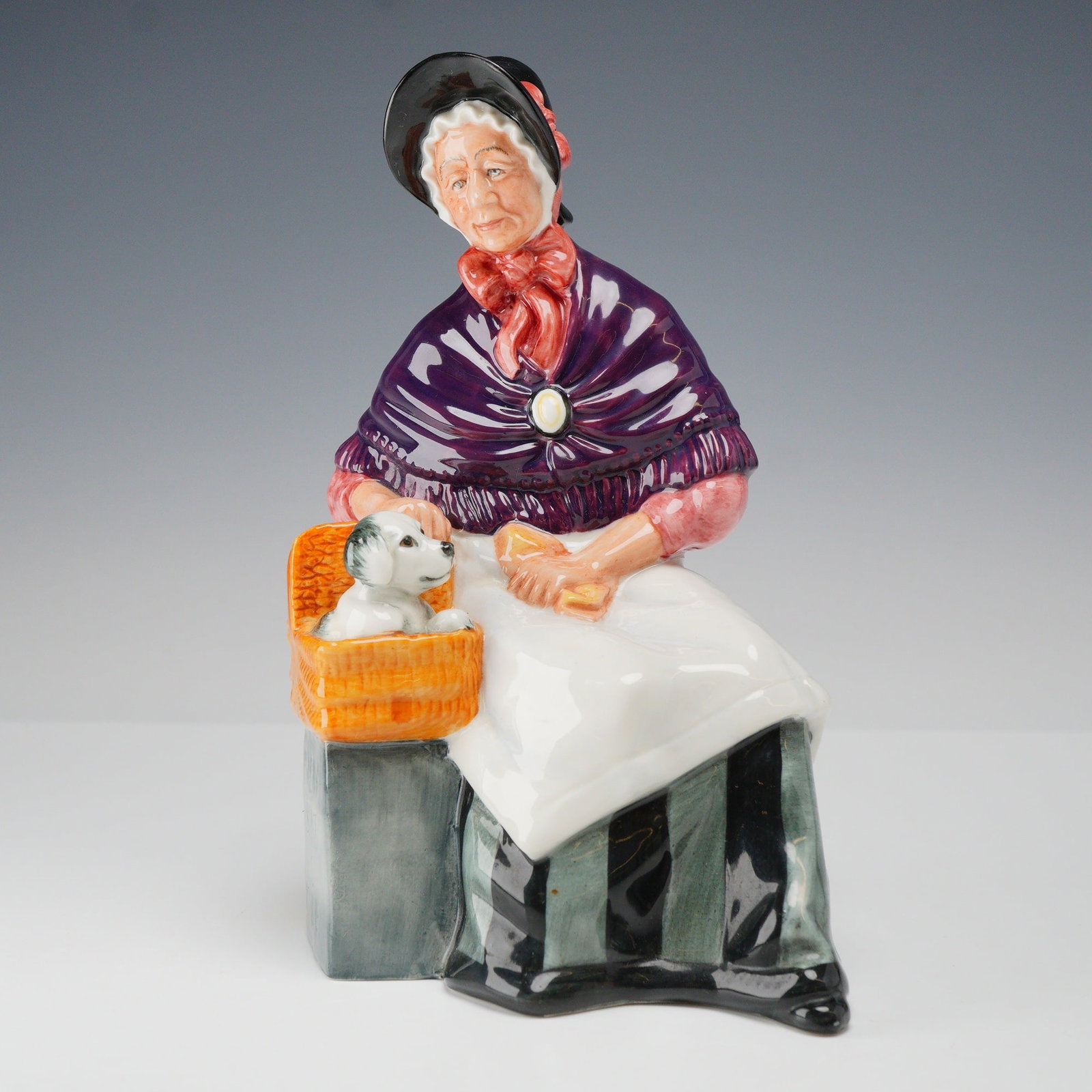Royal Doulton Porcelain Figurine, New Companions HN2770: A Royal Doulton fine bone china figurine titled New Companions, model HN 2770. The hand-painted figure depicts an elderly woman seated on a grassy mound, wearing a black bonnet over a white lace cap w